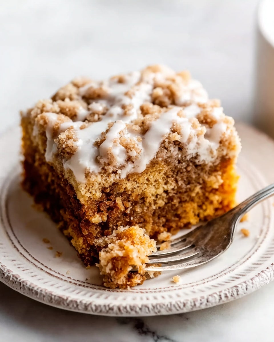 A square piece of crumb cake sits on a white plate with a textured round edge, placed on a white marbled surface. The cake has two layers; the bottom layer is a soft, moist, brown crumb cake with a close, fluffy texture, while the top layer is a crumbly streusel topping in a light golden brown color, uneven and chunky. A shiny white glaze drizzles unevenly over the crumble layer, creating a smooth contrast. A silver fork with a chunk of cake on it lies partly on the plate, showing the soft inside of the cake, with crumbs scattered around. photo taken with an iphone --ar 4:5 --v 7