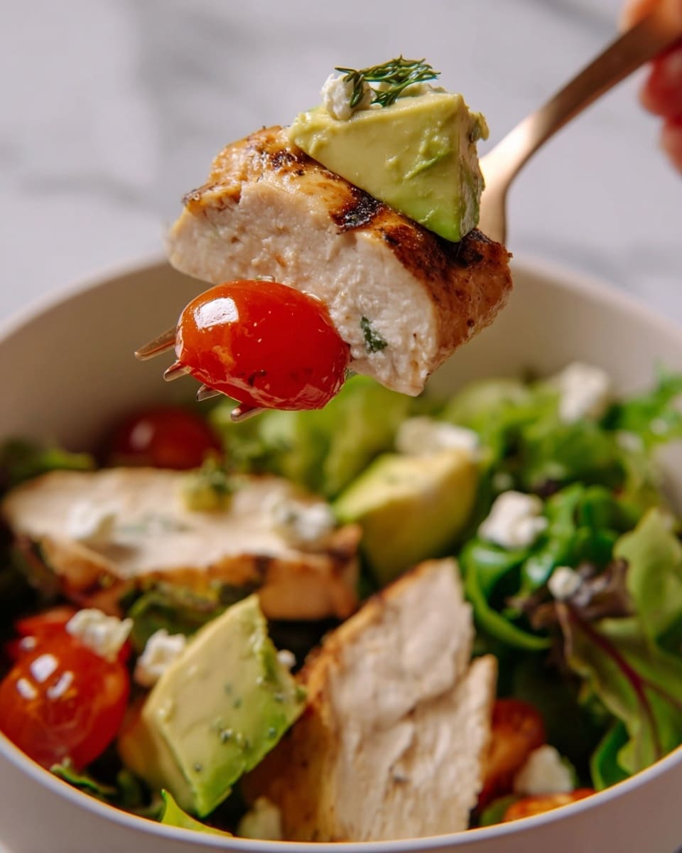 A fork held by a woman's hand lifts a bite of layered food showing three layers: a light brown grilled piece of chicken with a slightly charred edge, a pale green chunk of avocado with small white crumbles on it, and a bright red cherry tomato half nestled with some green leafy vegetables. In the background, a white bowl is filled with more slices of grilled chicken which are pale with crisp brown edges, and a mix of green leafy salad leaves and halved cherry tomatoes with a light dressing. The scene has a white marbled texture background. photo taken with an iphone --ar 4:5 --v 7