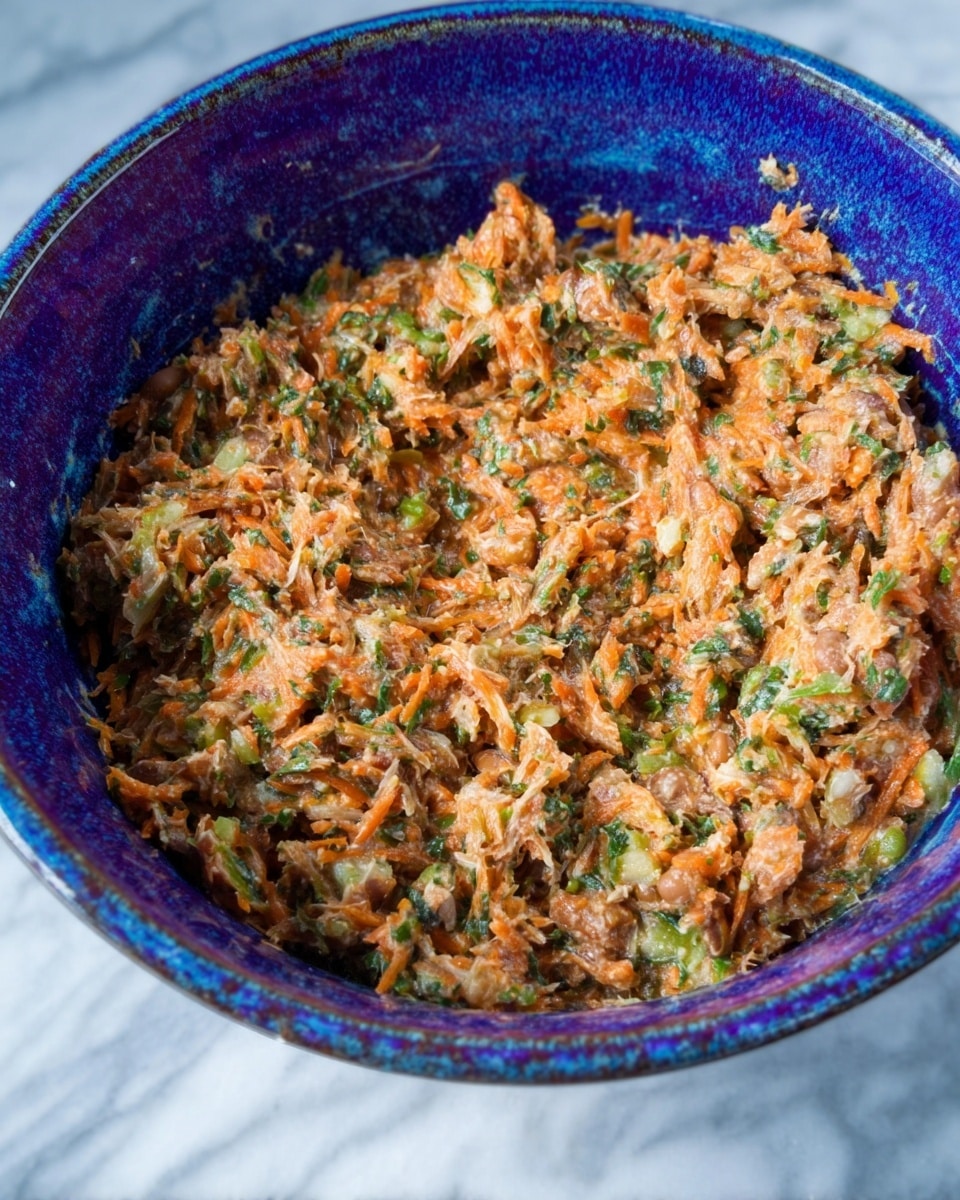 A close-up view of a thick, mixed salad placed in a white bowl with deep blue and purple inner glazing. The salad has a soft, mashed texture and is made up of finely shredded pieces in light brown, orange, and green colors, giving it a slightly rough but moist look. Bits of what seem to be grated carrot, chopped greens, and possibly beans or lentils are visible throughout. The bowl sits on a white marbled surface, adding a clean and bright background to the image. photo taken with an iphone --ar 4:5 --v 7