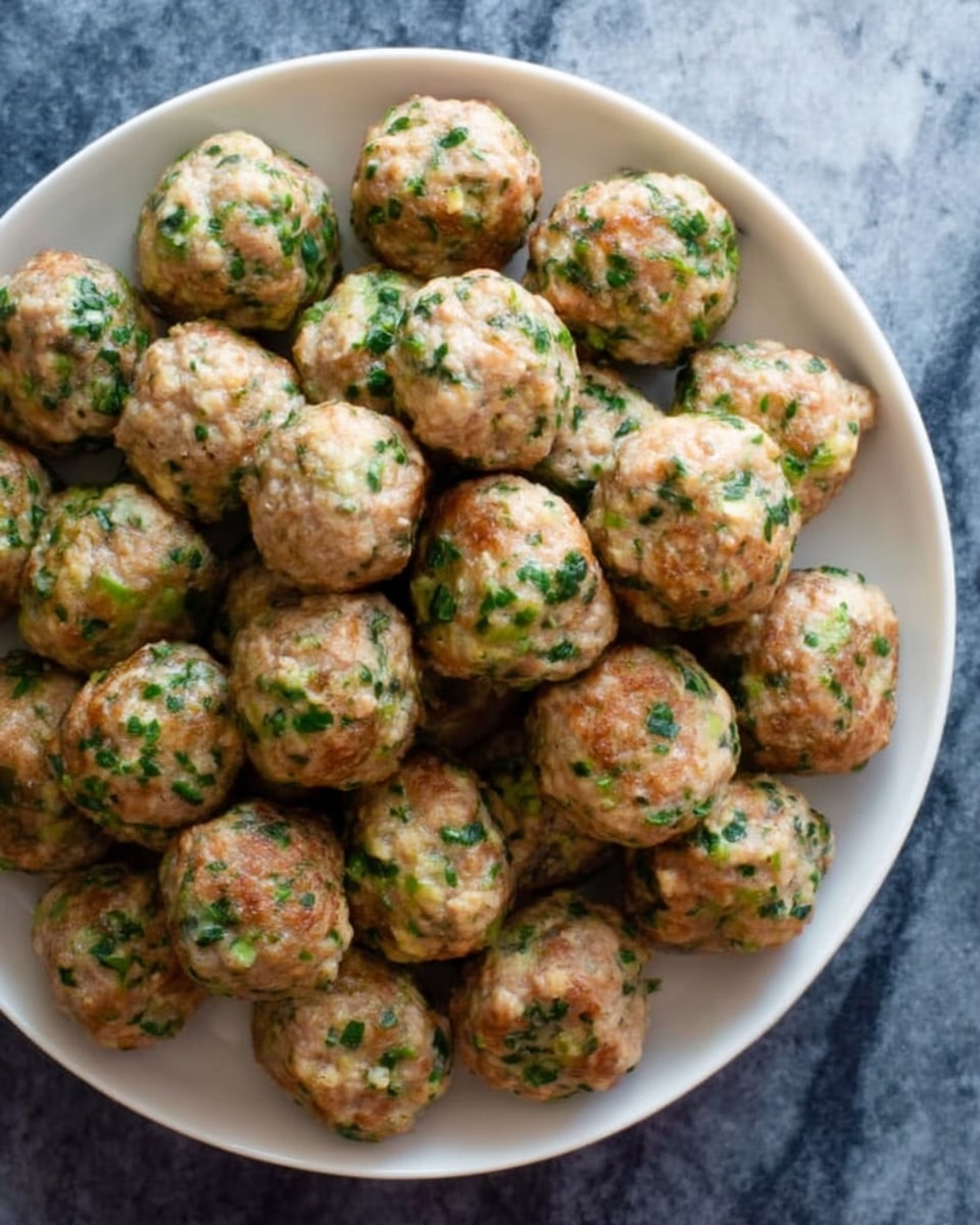 The image shows a white plate filled with small meatballs. Each meatball is round and has a light brown color mixed with green bits of herbs. The meatballs are piled up closely together, covering the whole plate. The plate is placed on a white marbled surface. Photo taken with an iphone --ar 4:5 --v 7