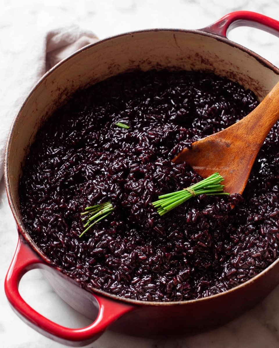 A close-up view of a thick, dark purple-black rice dish inside a red cast iron pot with two handles, sitting on a white marbled surface. The rice is shiny and sticky in texture, with two small green knots of herbs placed on top for garnish. A wooden spoon is partially dipped into the rice, with its tip covered in the thick mixture. Photo taken with an iphone --ar 4:5 --v 7