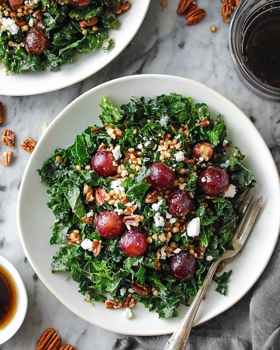 A white plate holds a fresh salad made of dark green leafy kale scattered evenly as the base layer. On top, there are shiny red grapes, crunchy light brown pecans, and small white crumbles of cheese spread throughout. Mixed in are golden grains of wheat or barley adding texture. A silver fork rests on the side of the plate. The plate sits on a white marbled surface with a small glass bowl of dark brown dressing and a few stray pecans and grapes around it. Another white plate with the same salad is partly visible in the background. Photo taken with an iphone --ar 4:5 --v 7