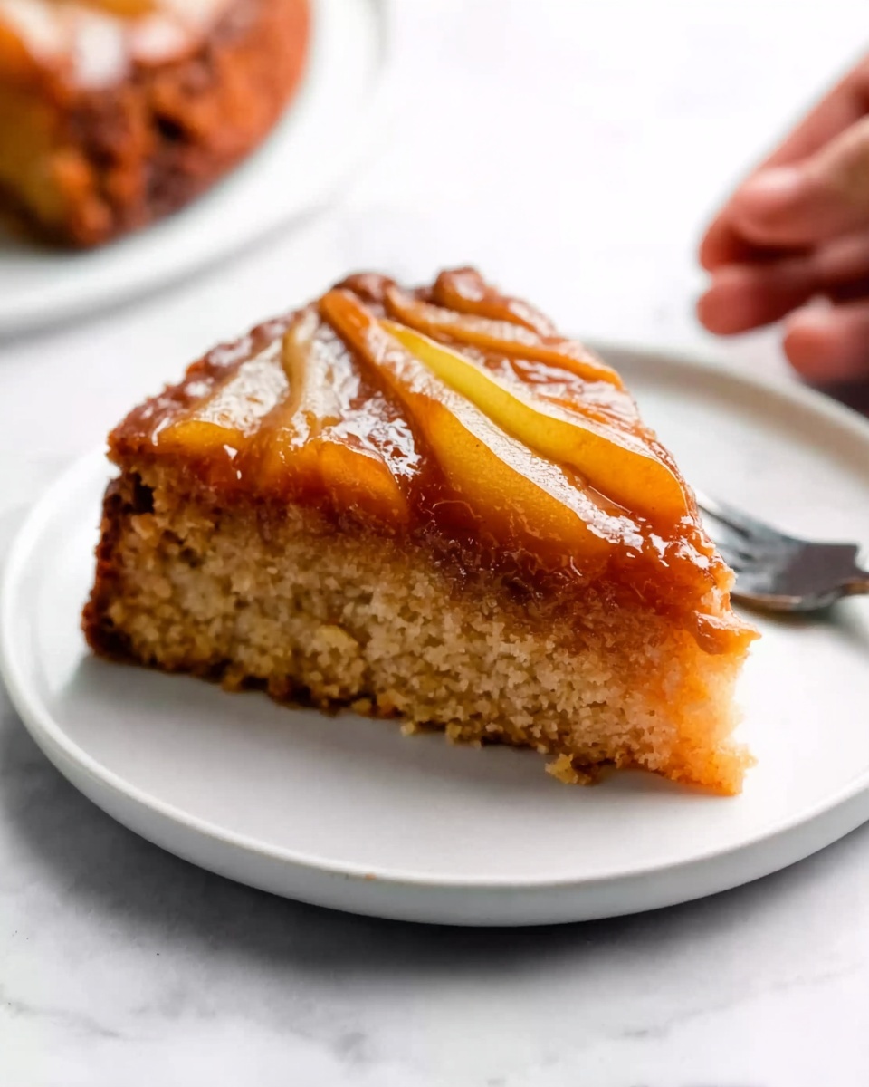 Caramel Apple Upside Down Cake Recipe 5 A single slice of upside-down pear cake is placed on a small white plate on a white marbled surface. The cake has three distinct layers: the bottom layer is a golden brown, soft, and moist cake base; the middle layer is a thick caramelized layer with a glossy, sticky texture; the top layer has three thin pear slices arranged side by side, covered in the same shiny caramel sauce. A woman's hand holds a fork in the background, ready to take a bite. Photo taken with an iphone --ar 4:5 --v 7