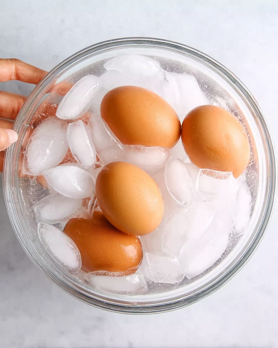 Air Fryer Hard Boiled Eggs Recipe 1 A black air fryer basket holds a single layer of twelve light brown eggs spread evenly across a textured black base. The basket is open and placed on a white marbled surface, with a wooden grinder nearby in the top left corner and a green cloth partially visible at the bottom left. The scene is lit with soft natural light, highlighting the smooth, oval shapes and matte texture of the eggs. Photo taken with an iphone --ar 4:5 --v 7