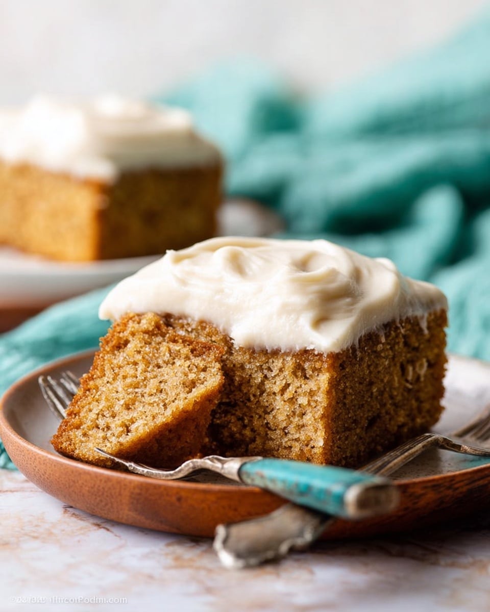 The image shows a single square piece of light brown cake with small specks inside, covered with a thick layer of creamy white frosting that has soft, smooth swirls on top. The piece is placed at the corner of a larger rectangular glass baking dish holding the rest of the cake, which has been cut into square sections. The clear dish sits on a white marbled surface with a teal cloth partially visible in the foreground. The lighting is soft and natural, highlighting the texture of the cake and the glossy finish of the frosting. photo taken with an iphone --ar 4:5 --v 7