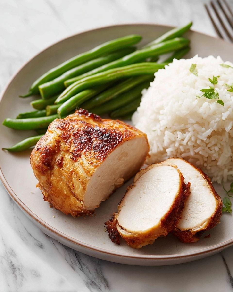 A white plate holds three main layers: on the bottom right is a fluffy mound of white rice with some black pepper on top, to the left of the rice is a small pile of shiny green beans arranged in a neat cluster, and in front is a piece of golden-brown roasted chicken with a crispy skin sprinkled with small bits of green herbs. In the background, three similar pieces of roasted chicken sit on a white plate with some juices and small herb bits scattered. To the right on the white marbled surface is a transparent amber glass filled halfway with dark liquid and a wedge of lemon inside. A gold fork and a green and white kitchen towel are partially visible on the left side. Photo taken with an iphone --ar 4:5 --v 7