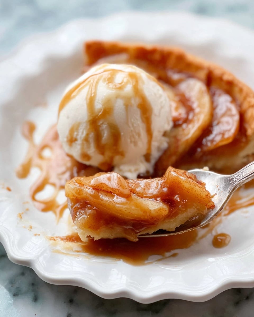 A round apple galette with a golden brown, flaky crust forming the outer layer, folded up unevenly around the edges. Inside the crust, there are thin apple slices arranged in a slightly overlapping circle, showing a warm light brown color from cinnamon seasoning. In the center, a scoop of white vanilla ice cream sits, melting slowly with some cream dripping down onto the apples, topped with a drizzle of shiny caramel sauce. The galette is on a white plate with a white marbled surface underneath. photo taken with an iphone --ar 4:5 --v 7