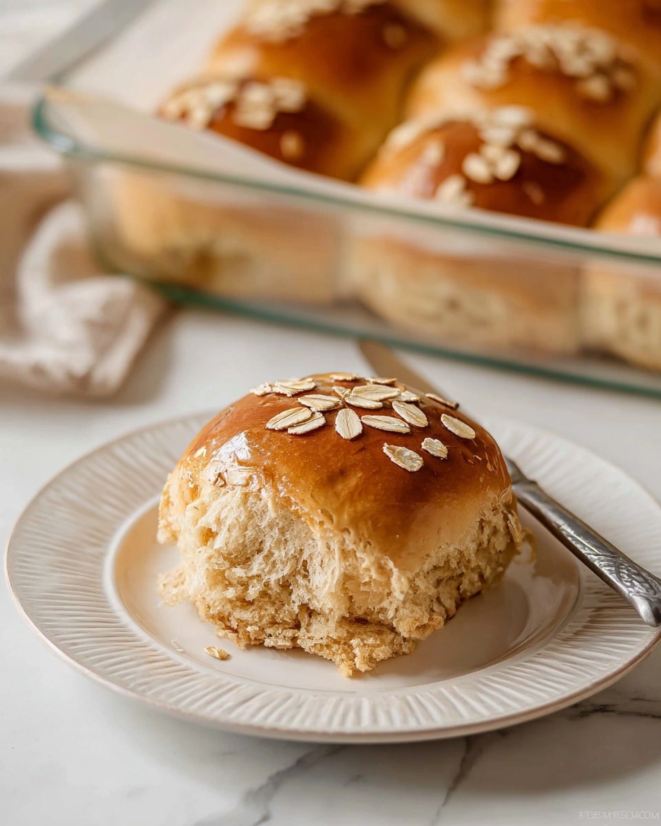 A glass baking dish lined with brown parchment paper holds a grid of sixteen golden brown soft rolls topped with scattered oats, showing a shiny, slightly textured surface. One roll at the bottom left corner is pulled apart, revealing a fluffy, light tan inside with a soft and airy texture. Surrounding the dish are small bowls of creamy white spread and a thick soup with yellow corn and herbs, all placed on a white marbled surface. To the left, there is a stack of white plates, and a butter knife with some spread on it lies nearby. A beige cloth with red stripes is laid on the bottom right. Photo taken with an iphone --ar 4:5 --v 7