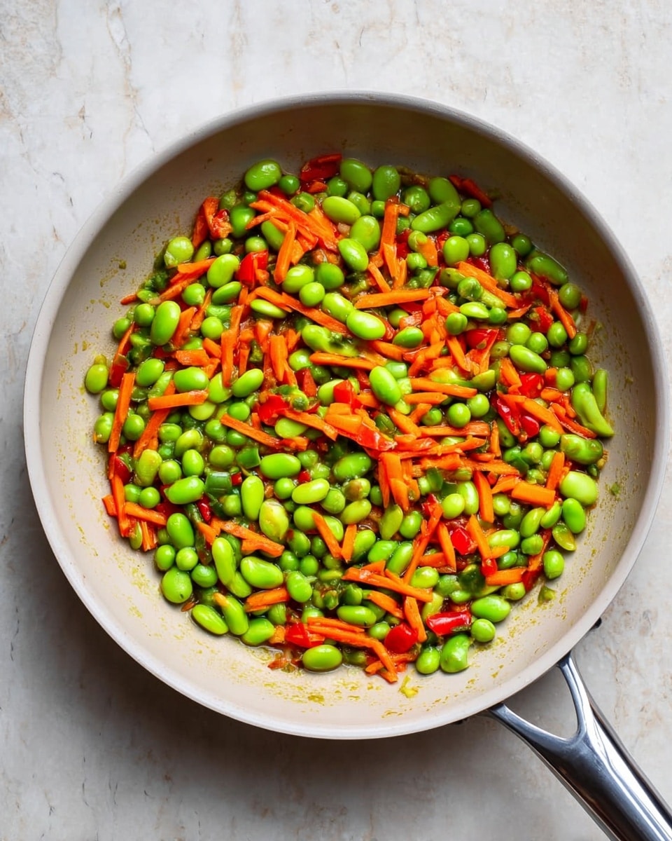 A white bowl filled with fried rice showing about four main layers: the base is light brown cooked rice mixed with small pieces of bright orange carrot, scattered green peas, and bright green chopped scallions. There are also small yellow pieces of scrambled egg spread throughout. The vegetables and egg are evenly mixed into the rice, giving a colorful, textured look that fills the bowl to the top. A metal spoon stands inside the bowl on the right side. The bowl sits on a white marbled surface near a small brown dish with red chili flakes and part of a blue and white striped cloth. photo taken with an iphone --ar 4:5 --v 7