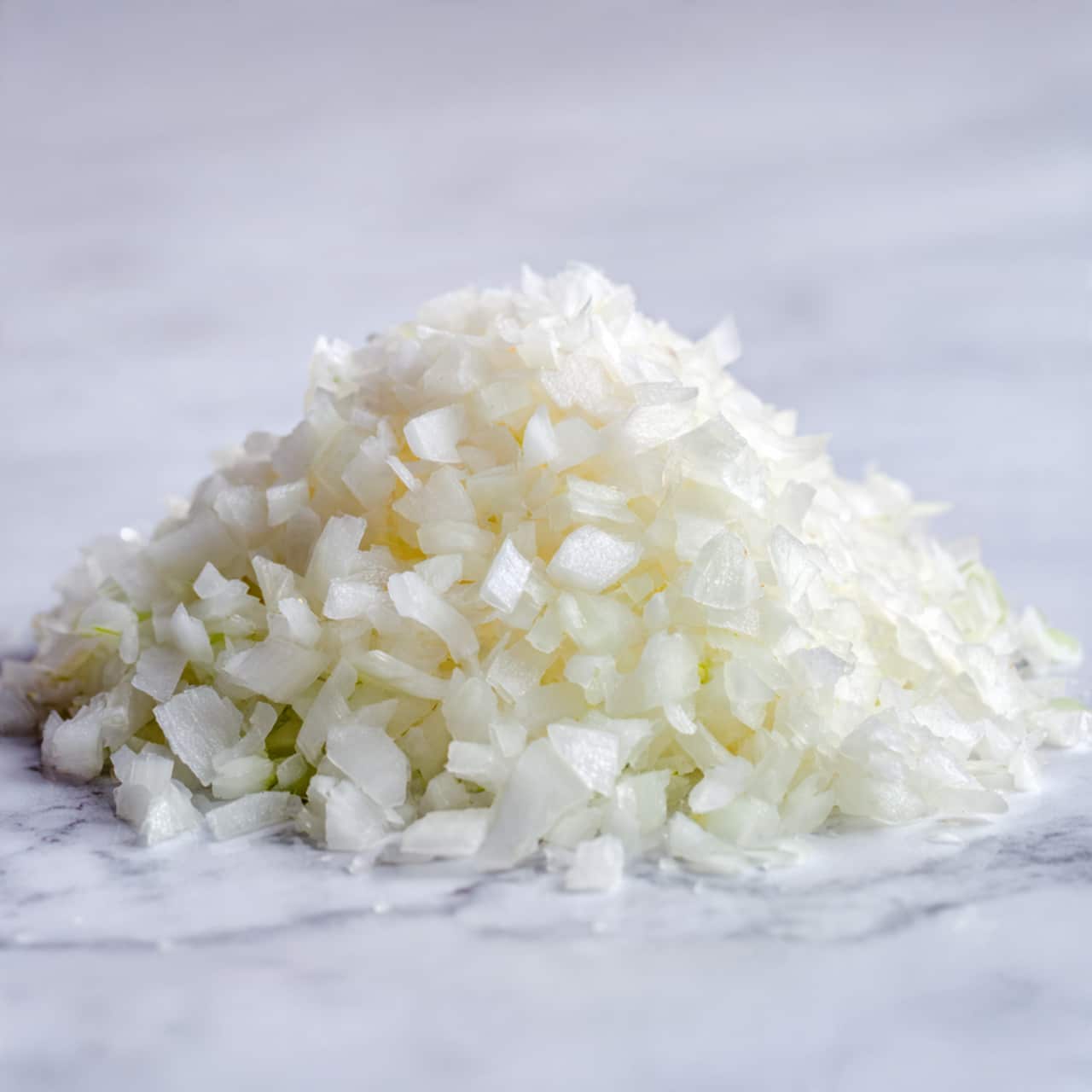 A close-up image showing a pile of finely chopped white onions on a white marbled surface. The onion pieces vary in size but are mostly small cubes and thin slices layered loosely together, with some translucent and shiny parts visible, showing freshness and moisture. The texture is crisp and slightly glossy, forming a light mound against the clean background. photo taken with an iphone --ar 4:5 --v 7