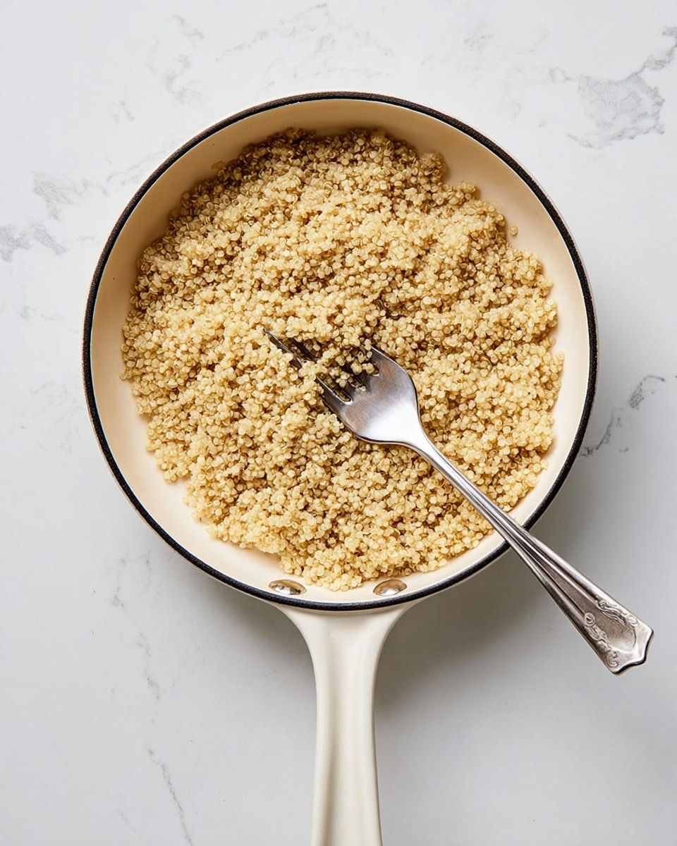 The image shows a close-up of a white pot filled with cooked quinoa. The quinoa grains are small, round, and light yellow with a fluffy texture. A silver fork is placed inside the pot on the right side, resting on the quinoa. The pot is set on a white marbled surface. photo taken with an iphone --ar 4:5 --v 7