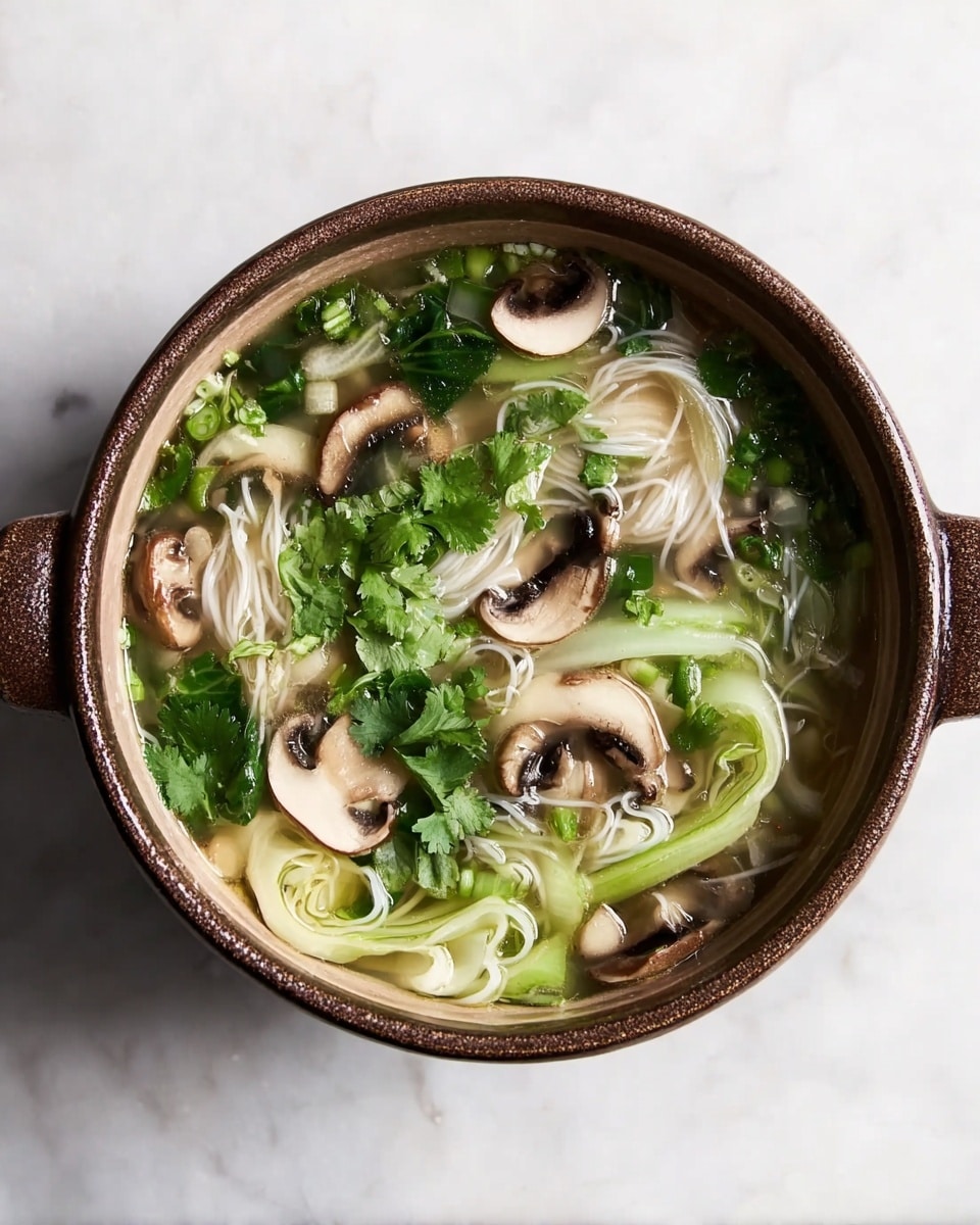 A round light brown pot filled with clear soup showing three main layers: the bottom layer with white noodles, the middle layer with light green sliced bok choy, and the top layer with whole and sliced brown mushrooms along with fresh green cilantro leaves floating in broth. The pot sits on a white marbled surface. Photo taken with an iphone --ar 4:5 --v 7