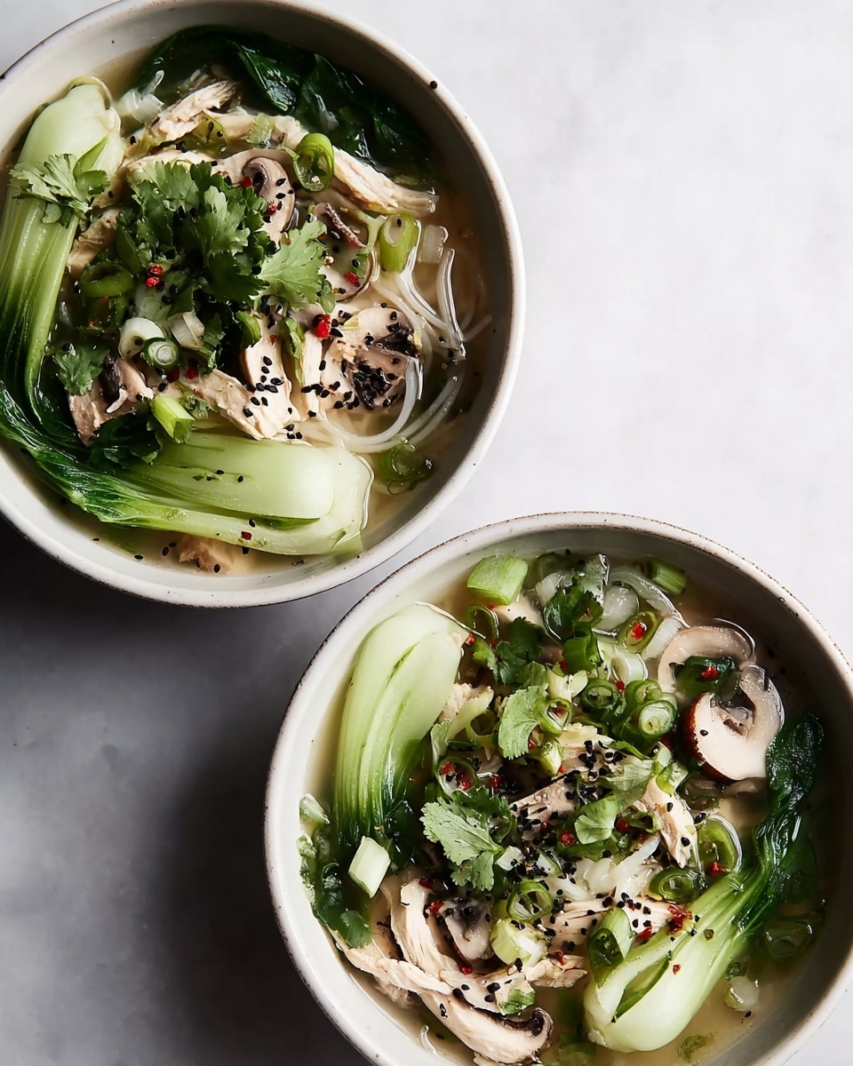 Two bowls of noodle soup on a white marbled surface, each white bowl filled with clear broth, thin white noodles at the base, topped with light green bok choy placed around the edges, soft beige slices of chicken scattered on top, light brown mushroom slices, fresh green cilantro leaves in the center, thin green onion pieces, sprinkled with black sesame seeds and small red chili flakes. photo taken with an iphone --ar 4:5 --v 7