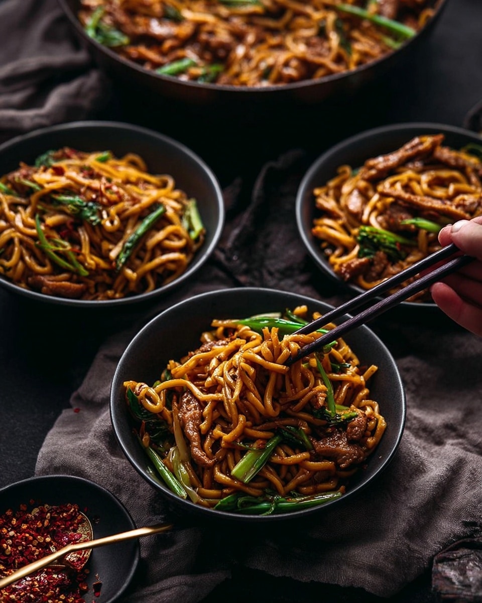 The image shows a dark pan filled with stir-fried noodles that are golden orange in color. The noodles are mixed with pieces of light brown chicken, sliced green vegetables, and topped with fresh green onion slices scattered across the top. Red and beige chopsticks are placed inside the pan, lifting some noodles. The pan sits on a dark surface with a grey cloth nearby and a small white bowl with a golden spoon holding some red chili flakes in the foreground. In the background, there are stacked brown bowls. The whole scene is set on a white marbled surface. photo taken with an iphone --ar 4:5 --v 7