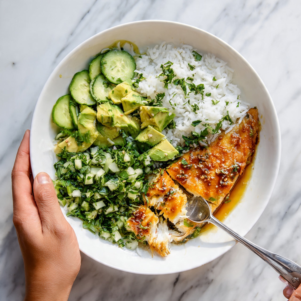 A white bowl filled with three main layers: at the bottom, a layer of green chopped cucumber and avocado mixed with herbs, showing a fresh and chunky texture; to the right, fluffy white rice resting next to the green layer; and on top, a long piece of cooked fish with a crispy, golden-brown surface, drizzled with a creamy light beige sauce that has slight browning and small dark spots. The bowl sits on a white marbled surface, with soft natural light highlighting the vibrant colors of the dish. Photo taken with an iphone --ar 4:5 --v 7