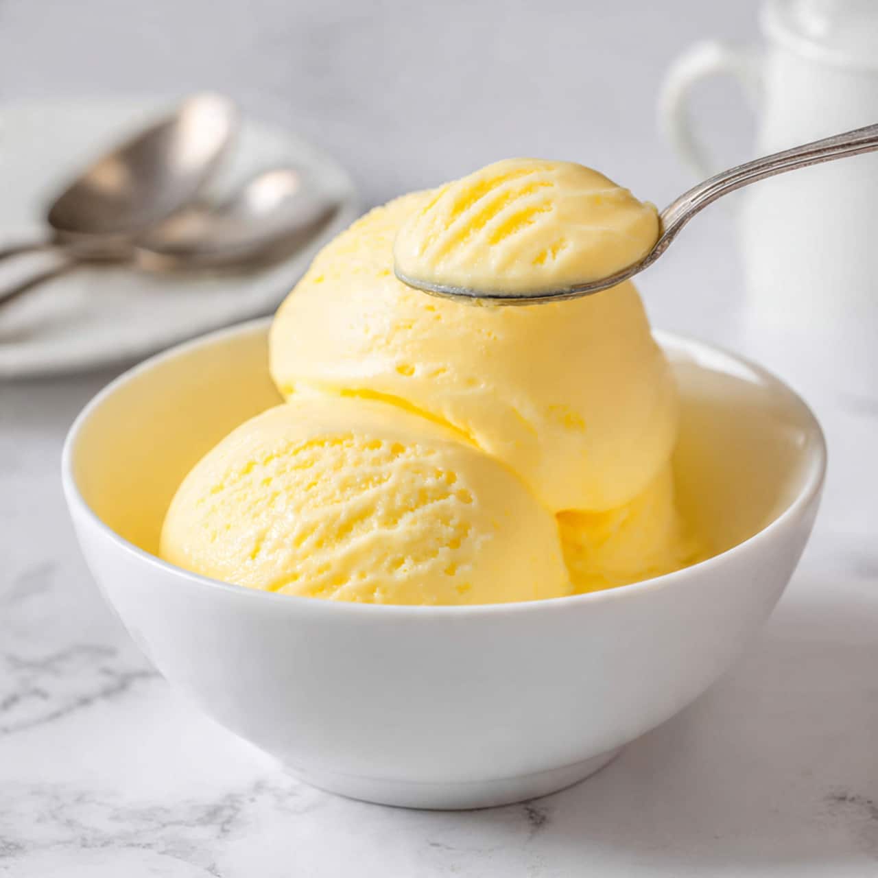 The image shows a round dessert with a smooth, creamy yellow top layer that covers the entire surface. Around the edge of the dessert, there is a ring of bright orange mango slices arranged neatly in two layers, slightly overlapping each other. In between and on top of the mango slices are small swirls of white whipped cream, placed evenly as decoration. The dessert is on a white plate, which rests on a light-colored cloth, all set on a white marbled surface. photo taken with an iphone --ar 4:5 --v 7