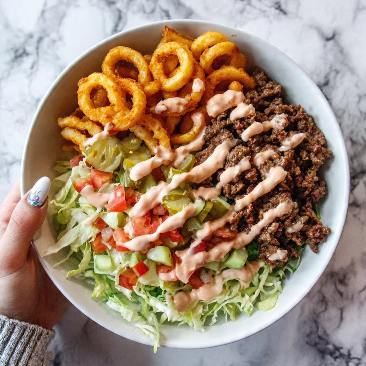 A white bowl filled with layers of food on a white marbled surface: at the bottom, light green shredded lettuce and bright red tomato pieces; above that, green sliced pickles; on top of the pickles, dark brown pieces of cooked meat; surrounding the meat, golden waffle fries; all covered with a light orange creamy sauce drizzled unevenly over the meat and fries. photo taken with an iphone --ar 4:5 --v 7