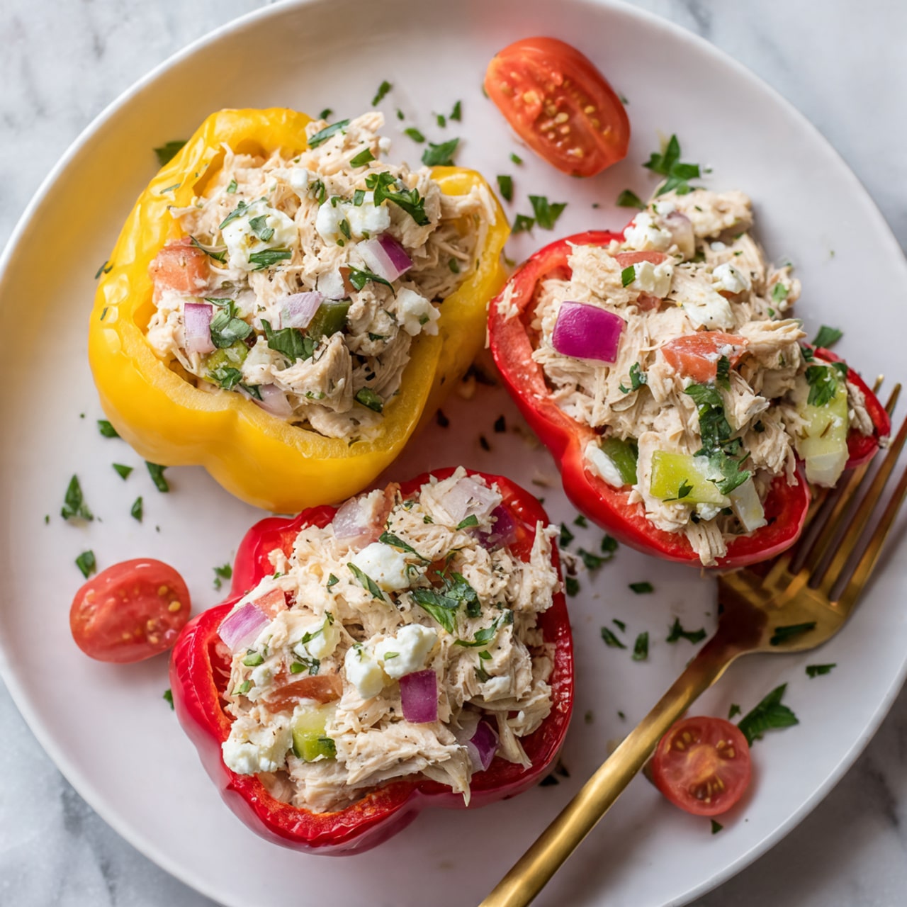 The image shows four stuffed bell pepper halves placed on a white oval plate with a subtle brown rim, set on a white marbled surface. Each pepper half is filled with a colorful mix including chunks of light beige cooked chicken, diced green zucchini, small red cherry tomato pieces, chopped green onions, and crumbled white cheese scattered on top. The bell peppers come in two colors: two bright red peppers on the sides and two yellow peppers in the middle, creating a vibrant contrast. There are small green herb leaves sprinkled over the filling for garnish. Around the peppers on the plate are small clusters of sliced orange and red cherry tomatoes and fresh green sprouts adding extra color and freshness. Photo taken with an iphone --ar 4:5 --v 7