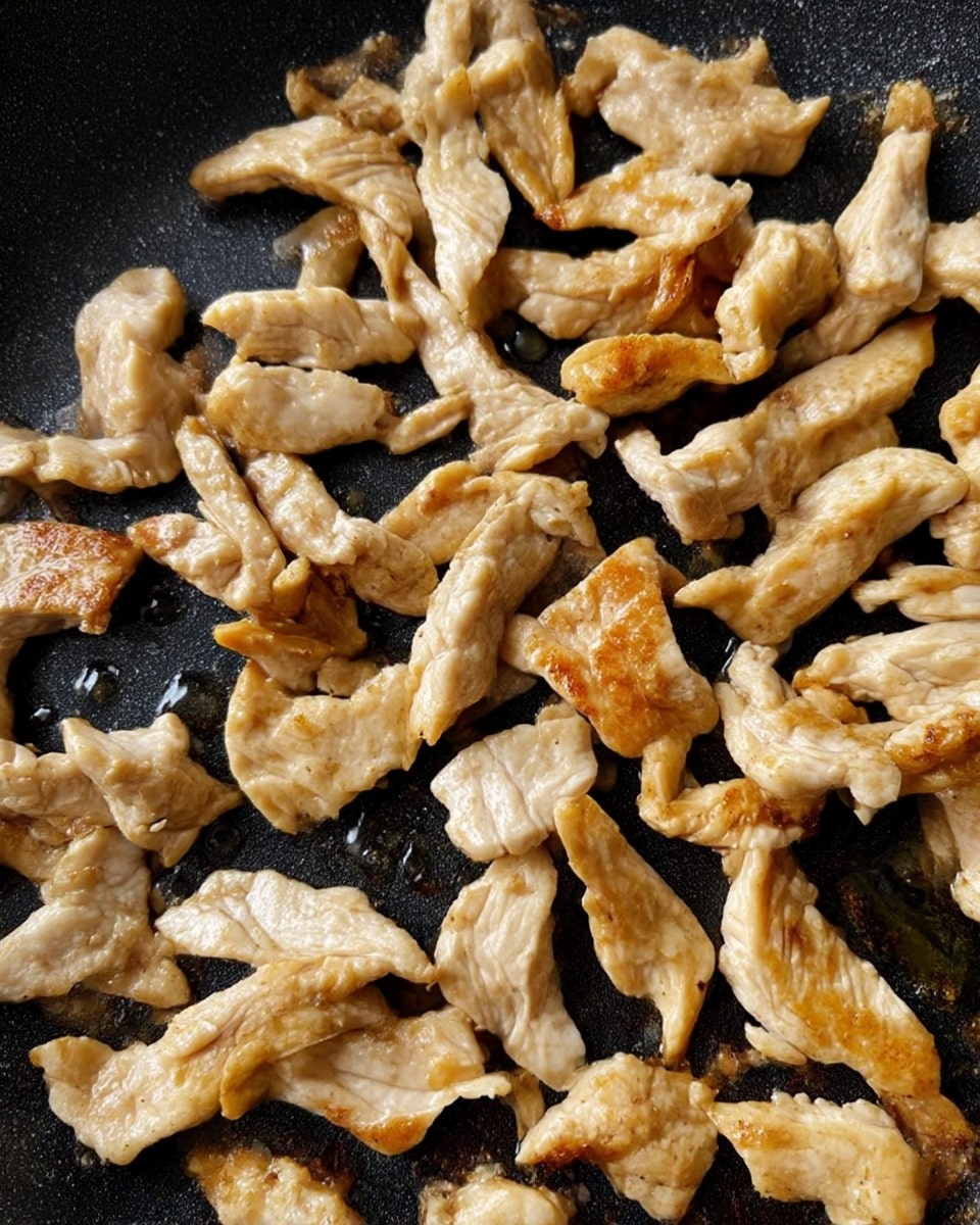 The image shows a close-up view of a creamy chicken and zucchini noodle dish in a pan. There are several pieces of light brown cooked chicken scattered throughout, mixed with thin spiral strands of green zucchini noodles. Mixed in are dark black olives and small pieces of reddish-brown sun-dried tomatoes. The creamy sauce is light beige and has some specks of black pepper sprinkled on top, giving the whole dish a slightly textured look. The background is a white marbled texture. photo taken with an iphone --ar 4:5 --v 7