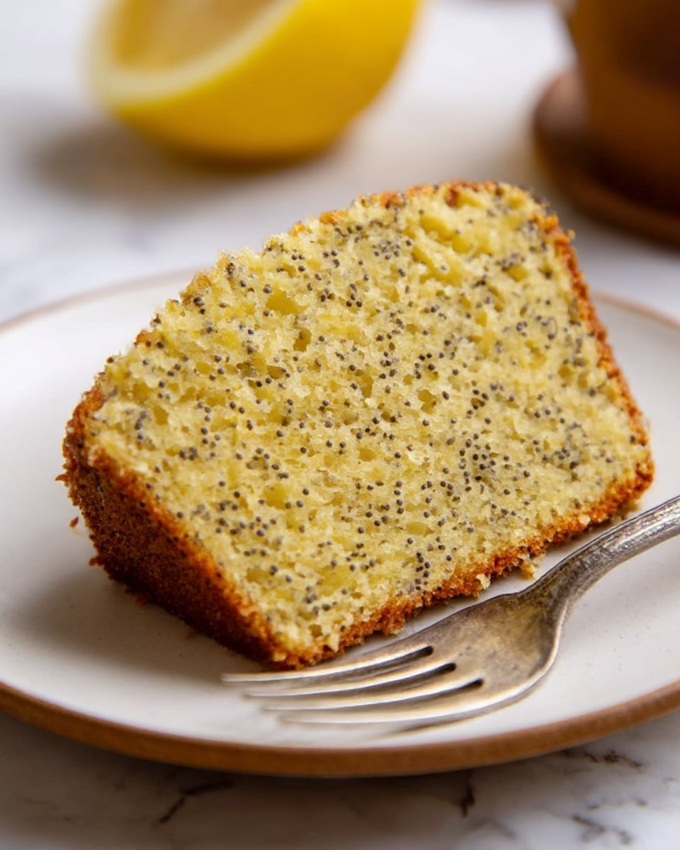 Two slices of yellow poppy seed cake with a slightly browned crust are each placed on round white wooden plates. The cake texture shows visible small black poppy seeds throughout, with a crumbly yet moist look. A shiny gold fork rests diagonally on the lower plate beside the cake slice. To the right side on the white marbled surface, a whole yellow lemon is placed. The scene is softly lit, creating a warm and inviting mood. Photo taken with an iphone --ar 4:5 --v 7
