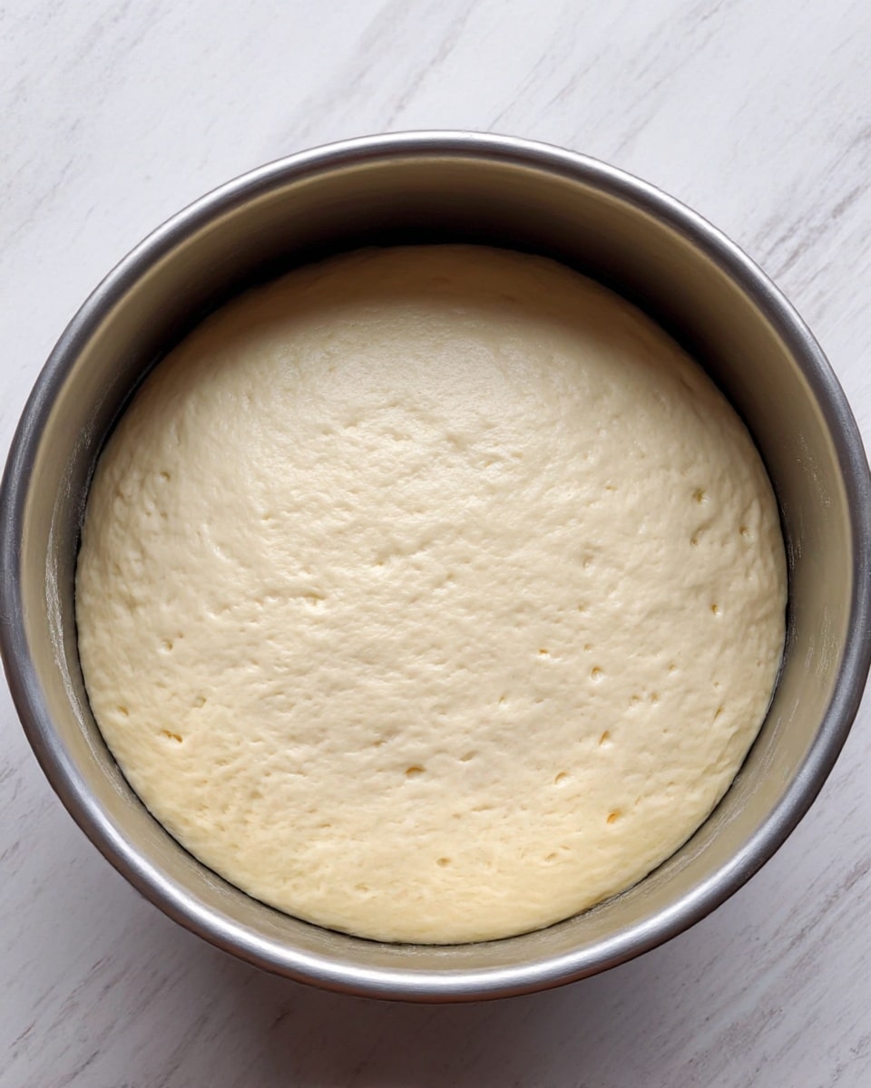 A round, golden-brown flatbread with a slightly uneven color pattern that shows darker toasted spots and lighter areas, held gently at the edge by a woman's hand on a wooden cutting board, the flatbread's surface looking soft yet cooked with a thin, smooth texture and slightly crisp edges, all set on a white marbled surface. photo taken with an iphone --ar 4:5 --v 7