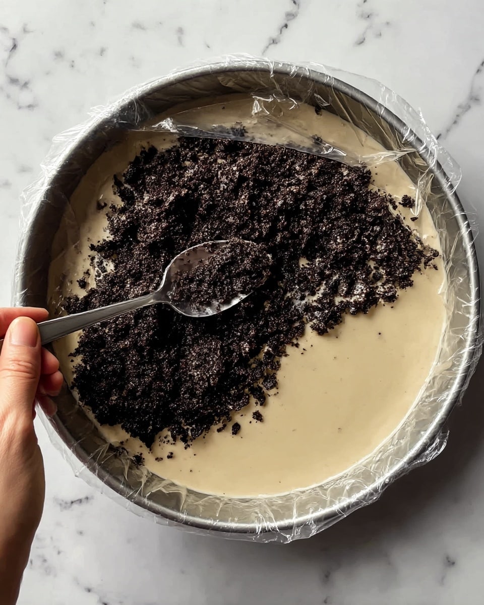 A slice of three-layered cheesecake sits on a white plate with a smooth, shiny light blue surface. The bottom layer is a crumbly dark brown crust with a rough texture. The middle layer is thick, creamy, and chocolate brown, looking soft and dense. The top layer is a pale cream color, smooth and matte, evenly covering the chocolate layer. On top, there is a small square piece of white and milk chocolate, placed near the wider edge of the slice. A golden fork lies beside the slice, with the tines pointing toward it. The background is a white marbled surface with subtle veins. Photo taken with an iphone --ar 4:5 --v 7