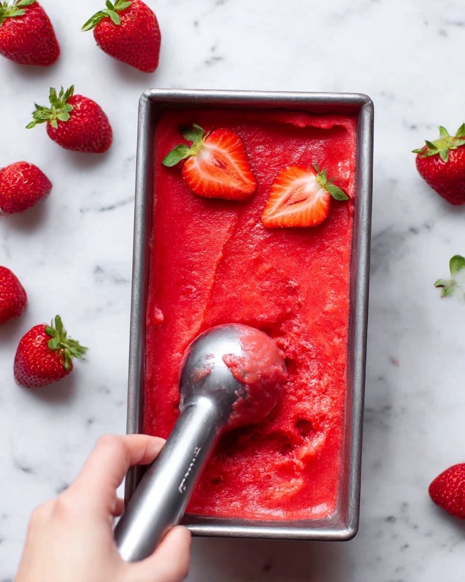 A metal rectangular container filled with bright red strawberry sorbet being scooped out by a woman's hand holding a metal ice cream scoop. Two fresh strawberry halves with green leaves are placed on the sorbet at the top corner. Around the container, whole strawberries with green tops rest on a white marbled surface. The sorbet has a smooth, creamy texture with some small chunks visible. The overall image shows a close-up view from above, focusing on the vibrant colors and freshness of the sorbet and strawberries. photo taken with an iphone --ar 4:5 --v 7