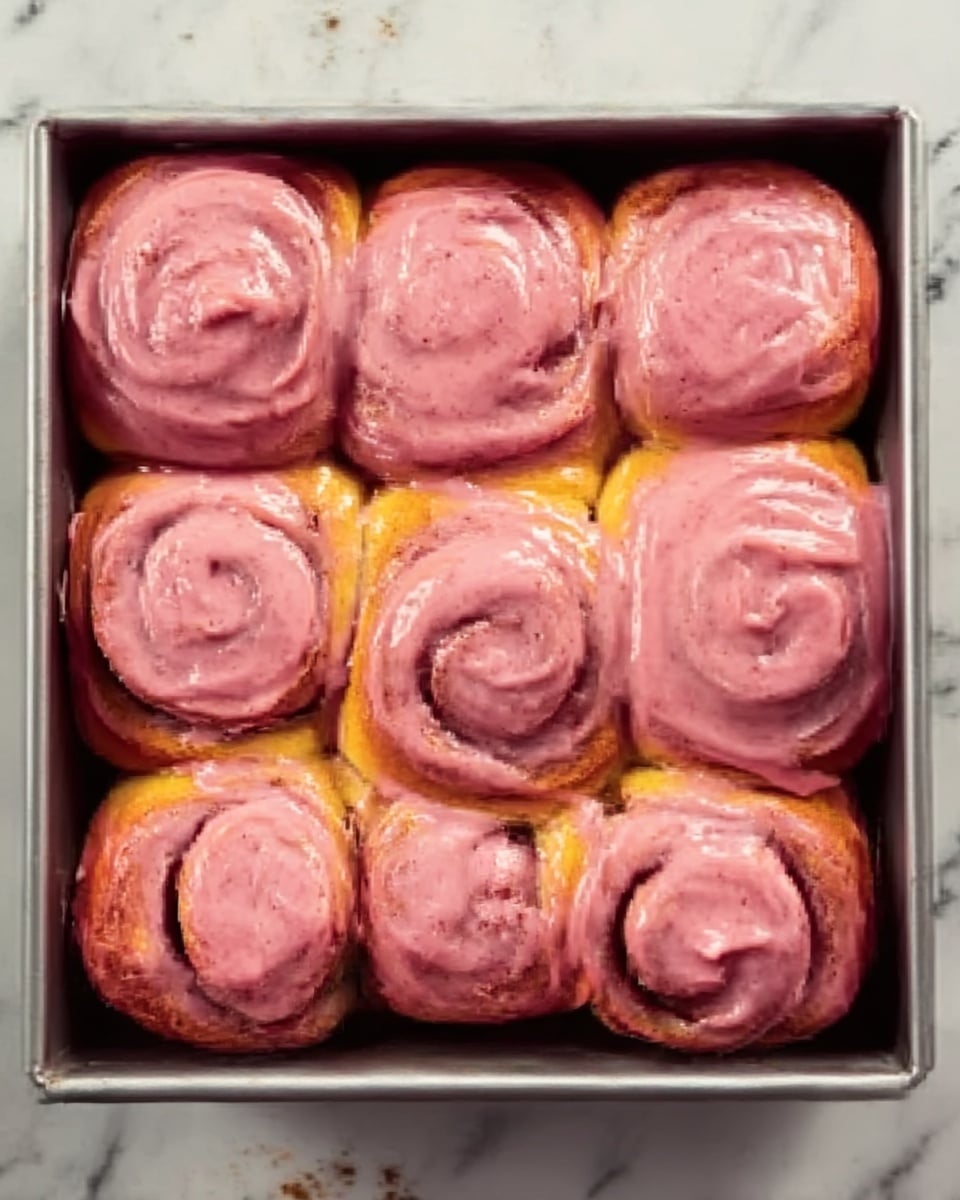 A single cinnamon roll is placed on a white plate, with a soft, light golden-brown base and a thick layer of smooth, pink glaze covering the top and sides. The roll has visible swirls, showing the fluffy, light texture inside with some strawberry specks in the glaze. In the background, a baking tray holds more cinnamon rolls covered with the same pink glaze, set on a white marbled surface. A few whole strawberries and a beige textured cloth are placed around the plate, adding bright red and soft neutral tones to the scene. photo taken with an iphone --ar 4:5 --v 7