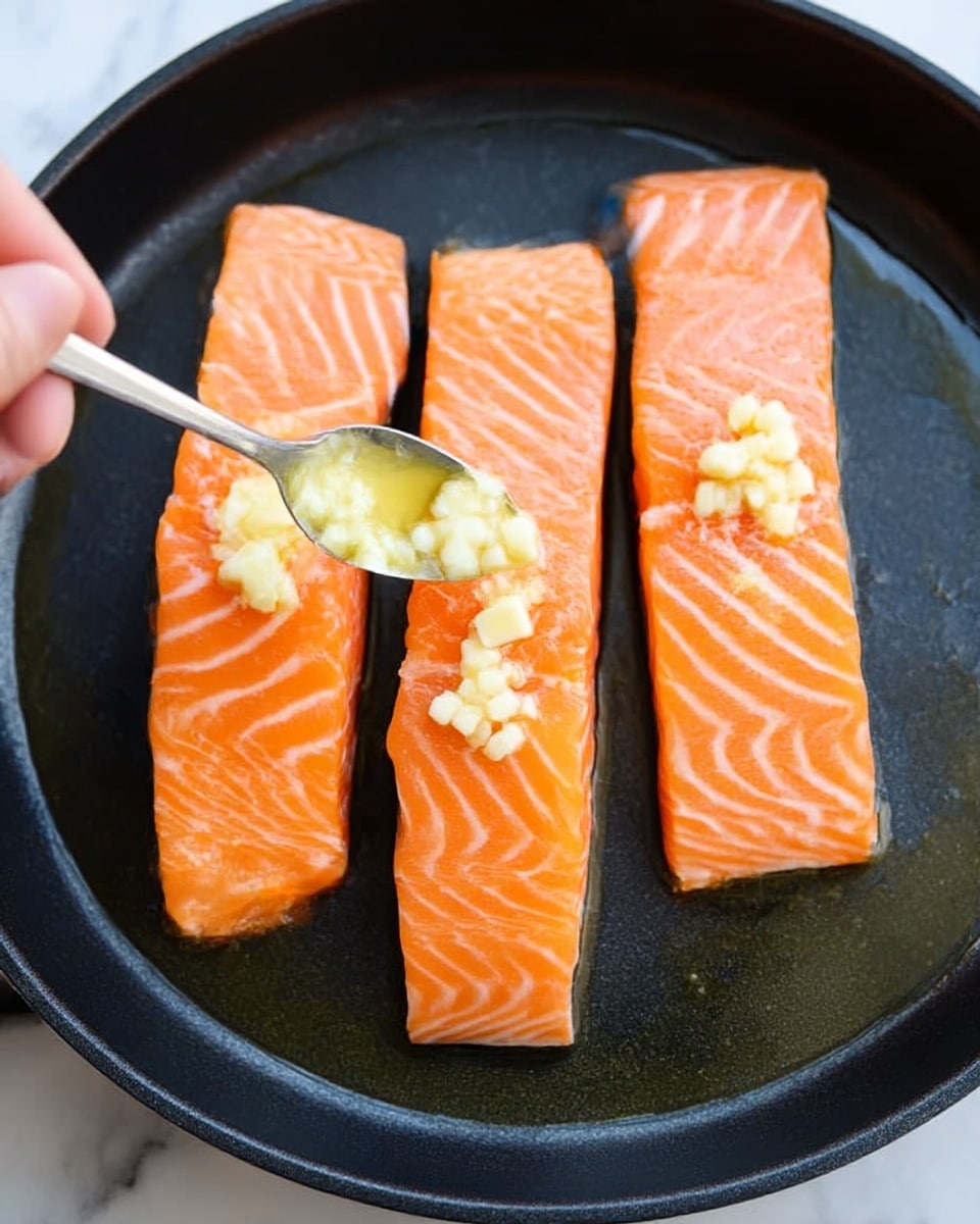 Four pieces of cooked salmon fillets with a golden brown crust are arranged in a row on a black pan. Each fillet has small bits of chopped garlic and sprinkled green onion on top, with a light texture of flaky cooked fish visible. Thin lemon slices are placed around the salmon for garnish, adding a pale yellow contrast. The background is a white marbled texture. Photo taken with an iphone --ar 4:5 --v 7