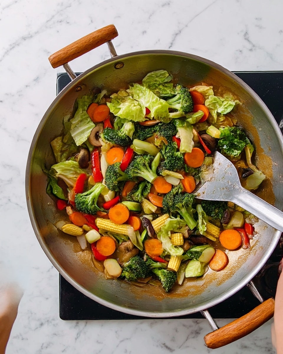 A large metallic wok with wooden handles is shown from above, filled with several layers of cooked vegetables. The bottom layer contains light brown liquid sauce spread evenly across the base. On top of that are bright green broccoli florets and slightly lighter green leafy napa cabbage pieces. Scattered among these are round orange carrot slices, red bell pepper slices, small yellow baby corn, and white thick onion chunks. There are also some pale green zucchini pieces and dark brown mushroom slices. A woman's hand is holding the wok handle on the left side while another woman's hand is using a large metal spatula with a long handle to stir the vegetables from the right side. The wok sits on a black stovetop, all placed on a white marbled surface. photo taken with an iphone --ar 4:5 --v 7