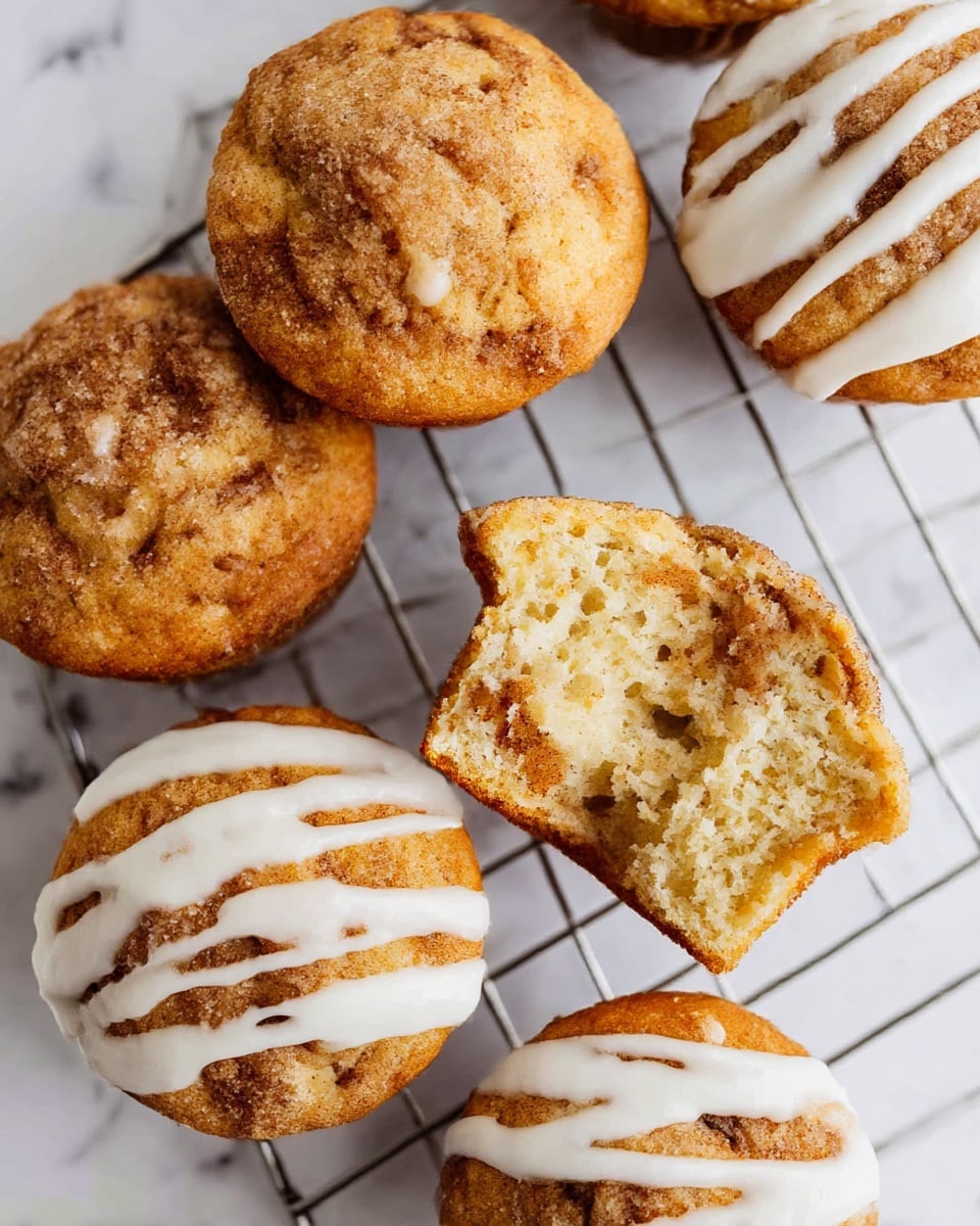 The image shows three muffins stacked on a soft white cloth on a white marbled surface. The top muffin is bitten, revealing a light, fluffy inside with some darker specks of cinnamon swirl. The muffins are golden brown with crumbly cinnamon topping. In the background, two glass bottles of milk are slightly out of focus. The overall feel is warm and cozy, with soft natural light. photo taken with an iphone --ar 4:5 --v 7