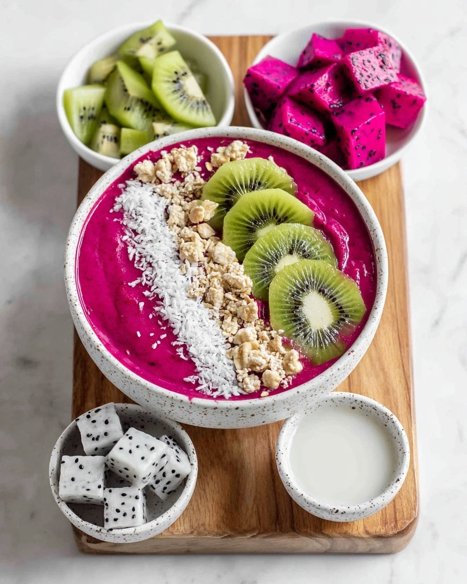 A white bowl filled with a smooth, thick bright pink creamy base takes up most of the space. On top of the pink cream, there are three main toppings arranged in separate sections: on the top right, three slices of green kiwi with dark seeds are placed close to one another; on the left side, medium-sized white cubes of dragon fruit with many small black seeds fill the space; along the upper left edge, there is a mix of white coconut flakes and small light brown granola pieces forming a textured border. The bowl sits on a white marbled surface with parts of another white bowl with kiwi slices visible at the bottom left edge. photo taken with an iphone --ar 4:5 --v 7