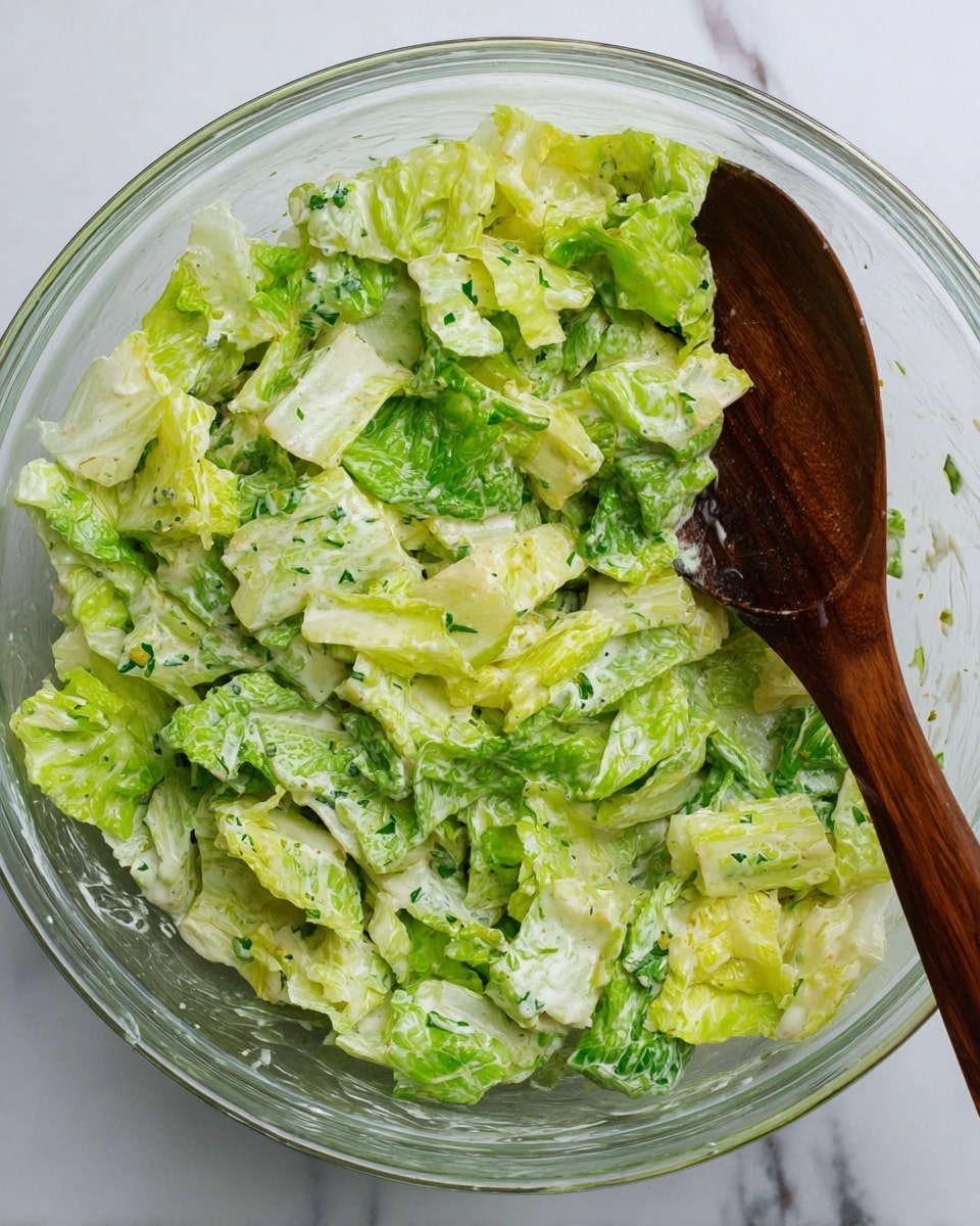 The image shows a fresh salad made of green and light green leafy lettuce mixed with small pieces of chopped green herbs, all lightly coated with a creamy dressing that has small black pepper specks. The mixture fills a white bowl, and the bright green colors of the lettuce contrast with the creamy white dressing. The texture looks crisp and fresh, and the salad appears well mixed with layers of soft and crunchy leaves. The background is a white marbled texture. Photo taken with an iphone --ar 4:5 --v 7