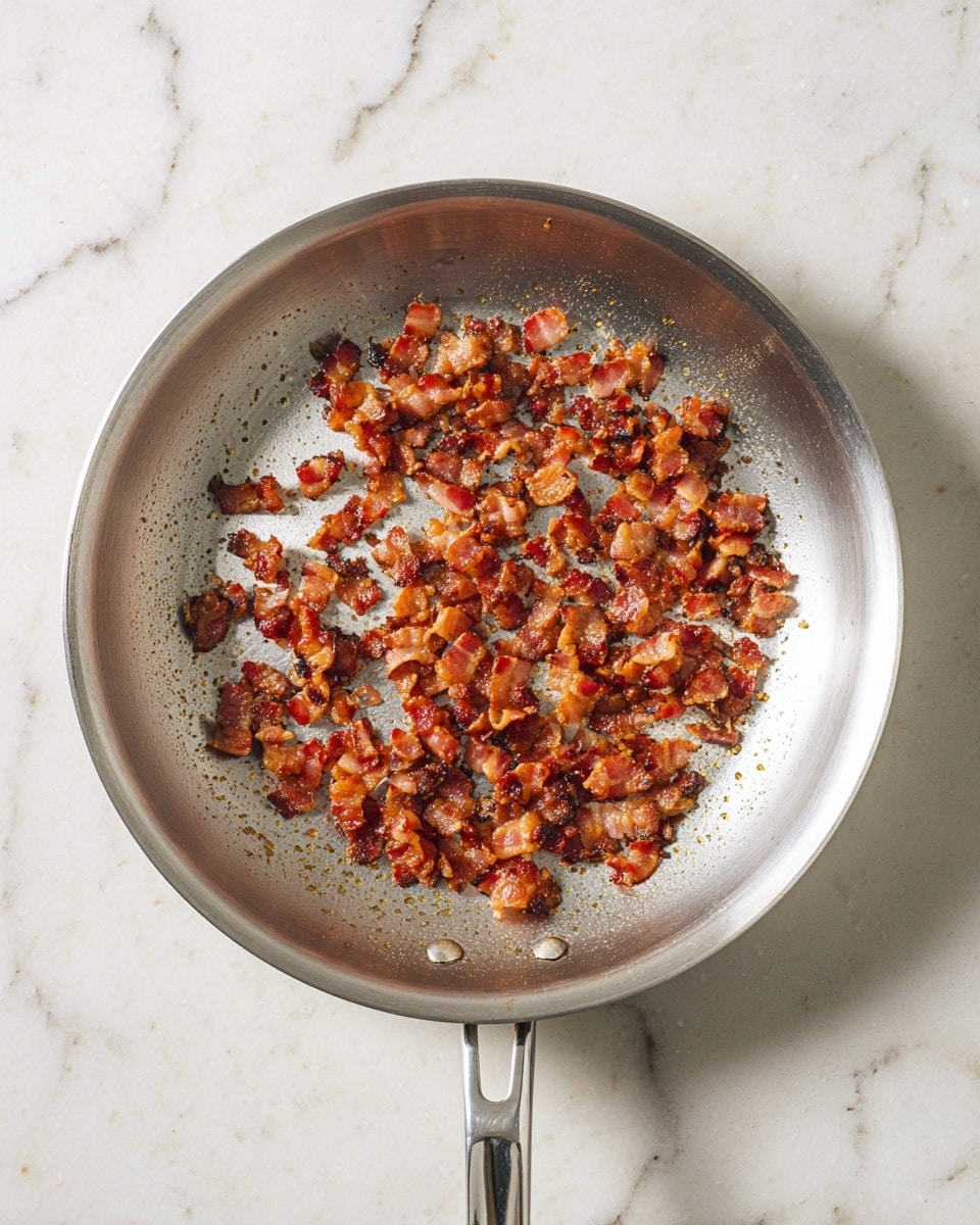 A round silver pan filled with small browned and crispy bacon pieces scattered evenly across the base, sitting on a white marbled surface. The bacon pieces show a mix of reddish-brown and golden colors with a slight shine from the cooked fat. The pan's smooth metal surface shows some signs of use with light marks and a reflective texture. The silver handle extends downward from the pan. Photo taken with an iphone --ar 4:5 --v 7