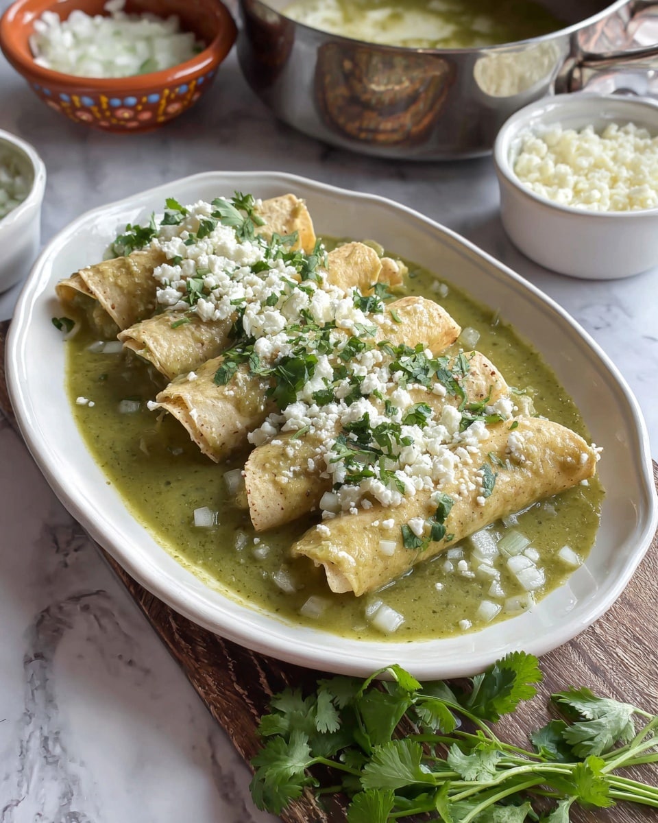 The image shows a white oval plate holding four rolled tortillas filled with a light beige filling, each covered in green sauce. The green sauce forms the bottom layer, spreading across the plate and providing a smooth texture. On top of the tortillas is a generous amount of white crumbly cheese sprinkled with small pieces of green cilantro. Fresh green cilantro is placed next to the plate on a wooden textured surface. In the background, there are small white bowls with some more cheese and onions, and a stainless steel pot is partly visible. The whole scene is set on a white marbled surface. photo taken with an iphone --ar 4:5 --v 7