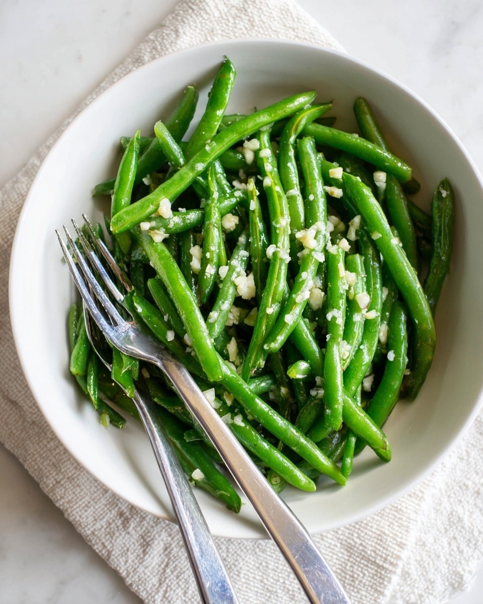 A black frying pan with a silver handle is filled with bright green, cooked green beans arranged loosely with some overlapping each other. A pair of silver tongs with black tips rests inside the pan, partly gripping a few beans. The background is a white marbled texture. photo taken with an iphone --ar 4:5 --v 7