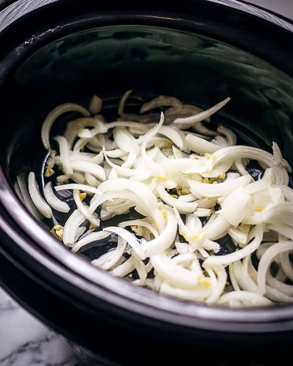 Inside a dark slow cooker, thin white onion slices with some small yellow bits are spread over the shiny black bottom. The onions are in curved strips, showing a slight shine as they sit layered evenly in one layer. The slow cooker has a glossy rim visible along the edge. The background is a white marbled texture. photo taken with an iphone --ar 4:5 --v 7