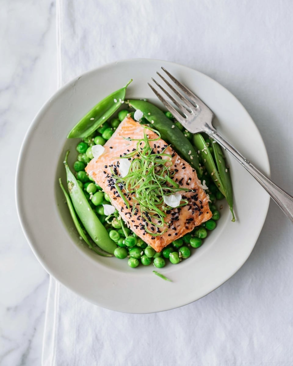 A white plate holds a piece of cooked salmon fillet with a light orange-pink color, topped with black sesame seeds and thin green vegetable curls with small white flowers. Underneath the salmon, there is a mix of bright green peas and snap peas spread evenly on the plate. A silver fork rests on the edge of the plate. The background is a white marbled texture. photo taken with an iphone --ar 4:5 --v 7