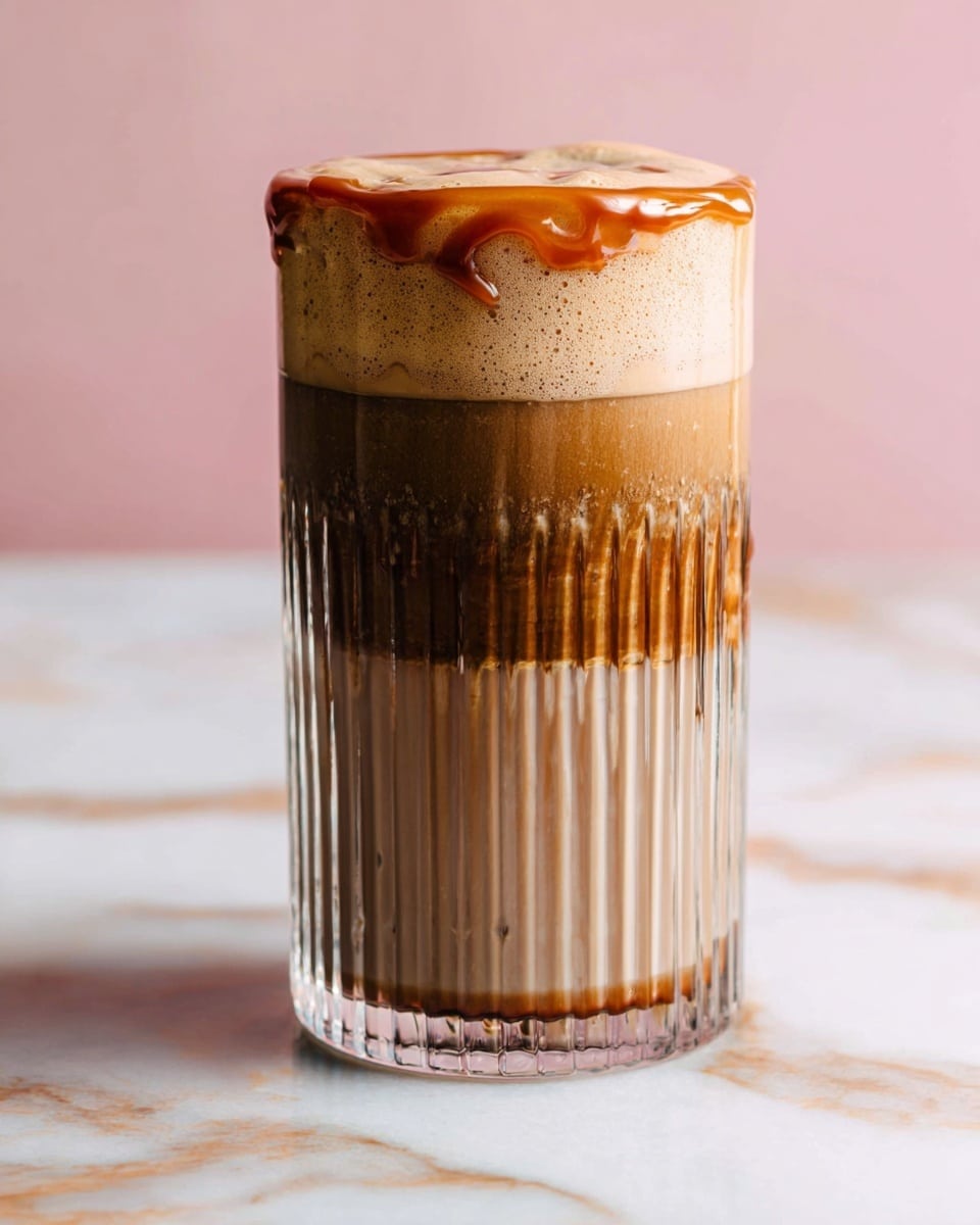 A tall, clear glass with vertical ridges shows a three-layer iced coffee drink placed on a white marbled surface, with a light brown frothy foam pouring and overflowing at the top. The bottom layer is dark brown, the middle layer is a medium brown mix, and the top layer is a light brown foam. Dark syrup drips in wavy lines along the inside edges of the glass, adding a textured contrast. The soft pink background adds warmth to the scene. photo taken with an iphone --ar 4:5 --v 7