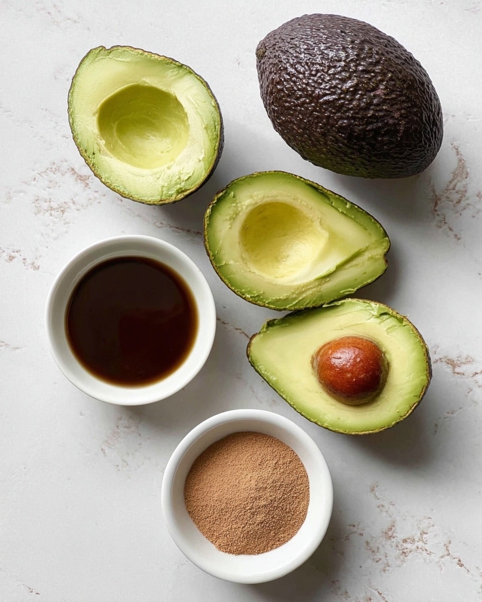 The image shows three avocados with dark green rough skin, two of them cut in half revealing a light green inside with one half having the large brown seed still in it. Below the avocados, there are three small white round bowls arranged in a triangle on a white marbled surface. The two bowls on the right side hold brown powdery cocoa and dark amber liquid honey while the bottom bowl is empty. The photo taken with an iphone --ar 4:5 --v 7