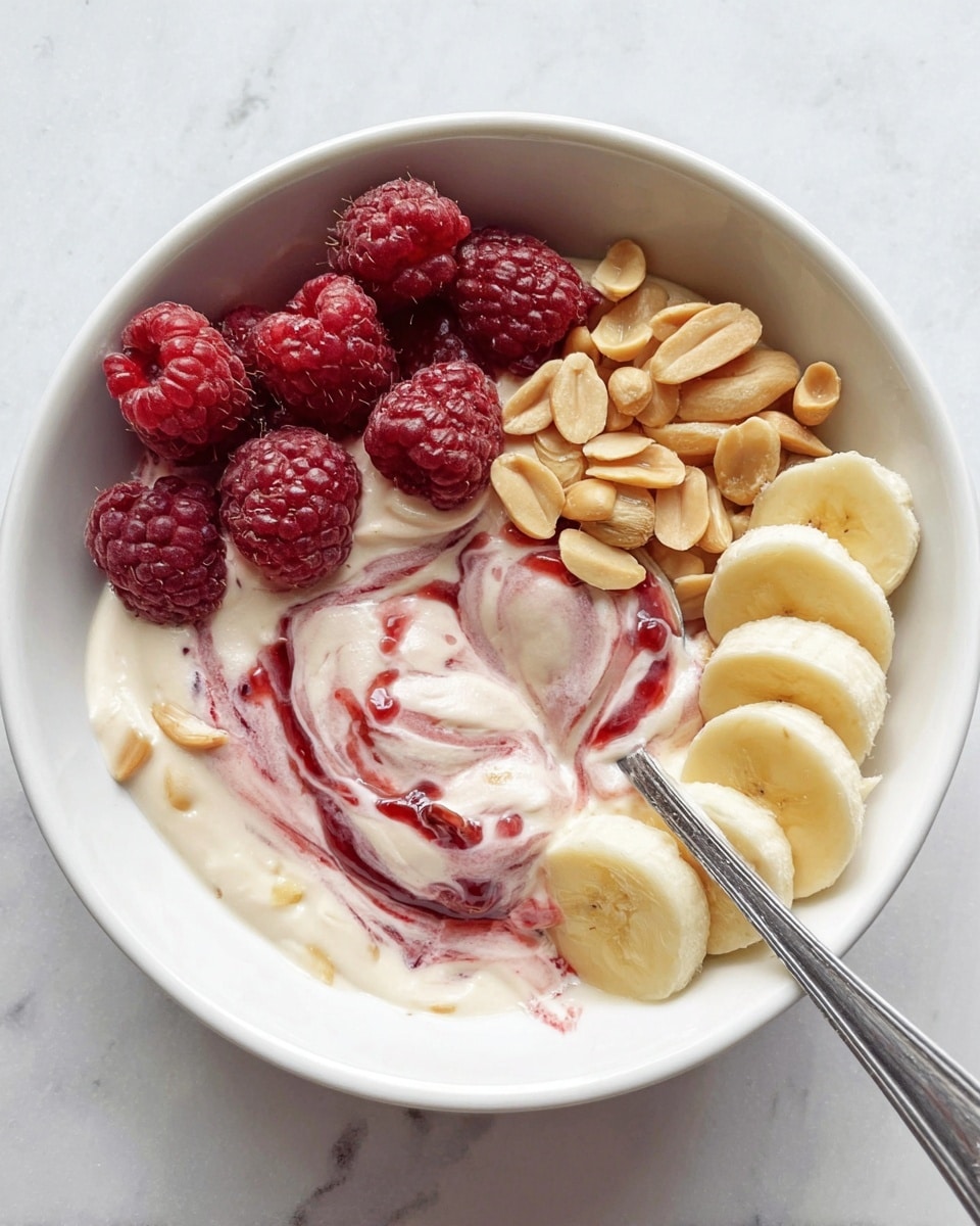 A white bowl filled with a creamy layer of yogurt swirled with red jam, topped with three curved rows of fresh fruit and nuts. On the top left, there is a row of bright red raspberries with a textured surface. Next to them, in the middle, is a small pile of light brown peanuts with a smooth and shiny texture. On the top right, a row of sliced banana pieces, pale yellow in color, curves along the bowl’s edge. A silver spoon rests on the right side, partially dipped into the yogurt and jam mix. The bowl is placed on a white marbled surface. Photo taken with an iphone --ar 4:5 --v 7