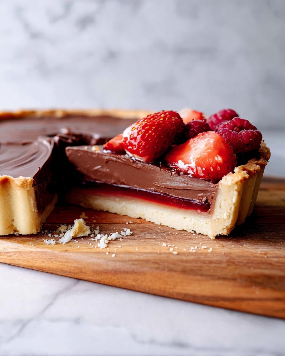 The image shows a sliced chocolate tart on a wooden board with a white marbled background. The tart has three clear layers: a light golden crust at the bottom, a thin deep red layer of jelly in the middle, and a thick, smooth dark chocolate filling on top. The tart slice on the right is topped with fresh strawberries and raspberries, with shiny red colors and juicy textures. The surface of the chocolate layer is smooth with slight swirls, and there are some crumbs scattered near the base of the tart, adding a rustic feel. Photo taken with an iphone --ar 4:5 --v 7
