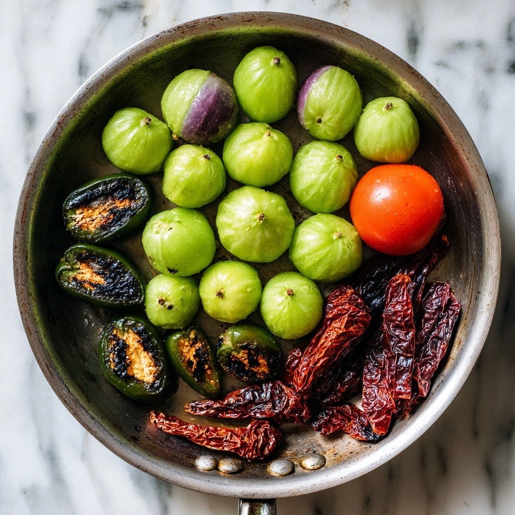 The image shows a metal pan on a white marbled stove surface filled with fresh vegetables. There are about twenty green tomatillos, some of them with purple spots, spread across the top half of the pan. Near the center bottom, there is one bright red tomato with a shiny surface. On the left side of the pan, there are six dark green jalapeño peppers, with three of them sliced in half revealing some charred black marks inside. On the right side, there are four dried red chili peppers with wrinkled skin and darkened charred spots. The pan surface shows some dark marks indicating cooking use. Photo taken with an iphone --ar 4:5 --v 7