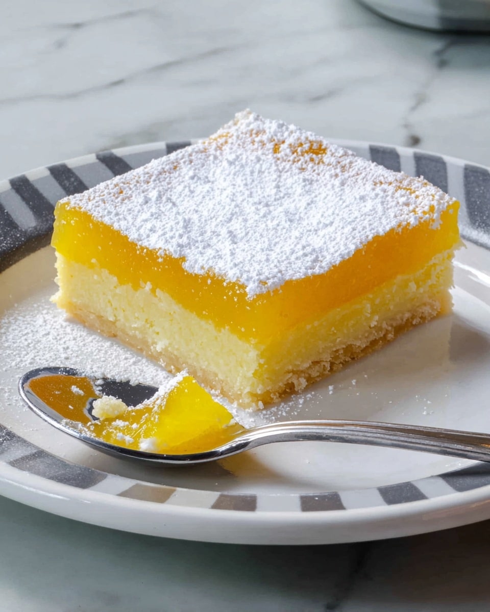 A square lemon bar dessert with two layers sits on a white plate with gray stripes and a thin black rim, placed on a white marbled surface. The bottom layer is a pale yellow, crumbly crust. The middle layer is bright yellow, smooth lemon filling. The top layer is a dusting of white powdered sugar evenly spread. In the background, a metal baking pan with more lemon bars cut into squares is visible. Photo taken with an iphone --ar 4:5 --v 7