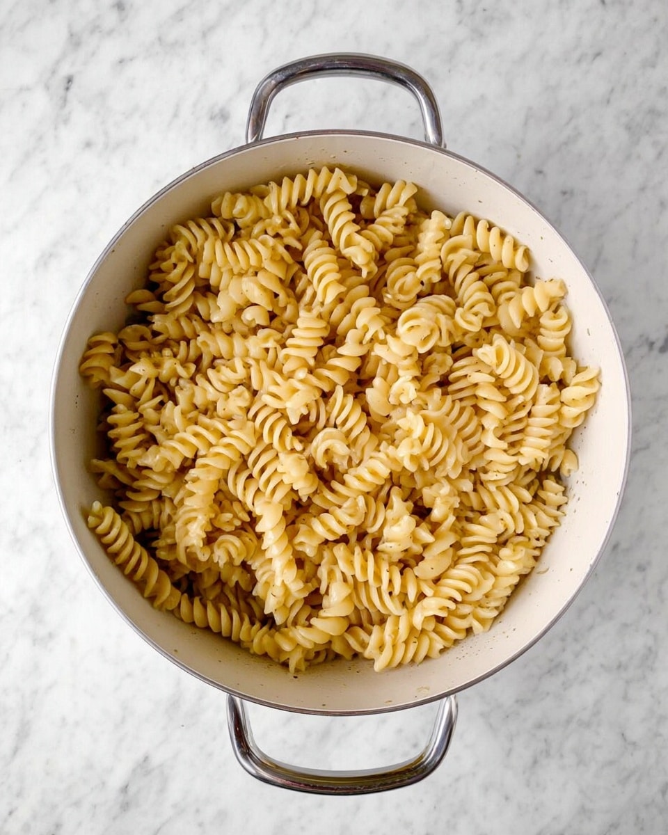 A close-up of a white bowl filled with three layers: at the bottom, light yellow rotini pasta with a soft texture, mixed with bright green peas scattered evenly; the middle layer consists of small white crumbles of cheese spread throughout; the top layer is sprinkled with finely chopped green herbs, giving a fresh look. A silver fork is inserted into the pasta, lifting a mixed bite of pasta and peas from the bowl. The bowl is placed on a white marbled surface. photo taken with an iphone --ar 4:5 --v 7