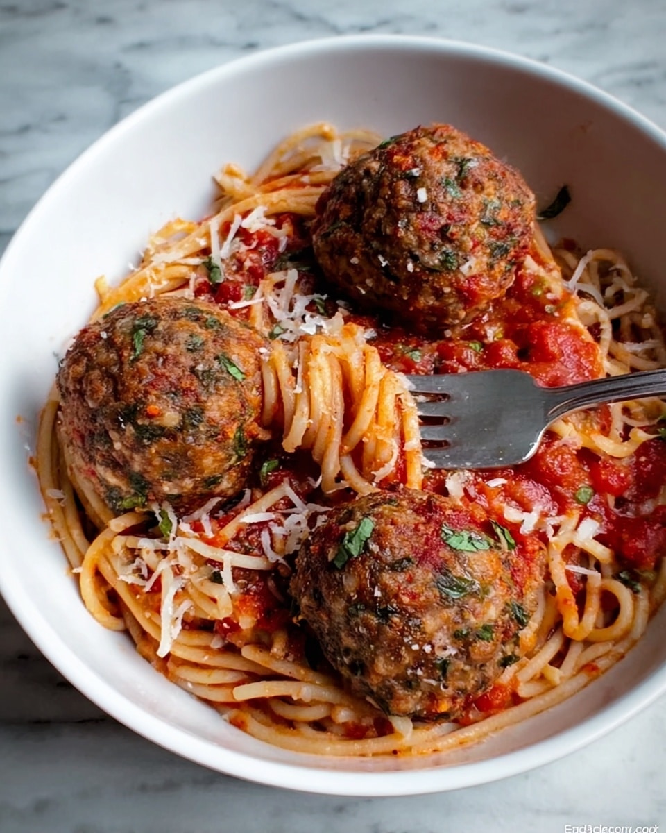 A white bowl filled with three large round meatballs placed on a bed of cooked spaghetti noodles mixed with red tomato sauce. The meatballs have a textured surface with small visible bits of green herbs and darker spices. The spaghetti is lightly coated in the sauce, with small chunks of tomato visible. Some thin white shredded cheese is sprinkled over the meatballs and spaghetti. A silver fork is resting inside the bowl, partially inserted among the noodles. The bowl is placed on a white marbled surface. photo taken with an iphone --ar 4:5 --v 7