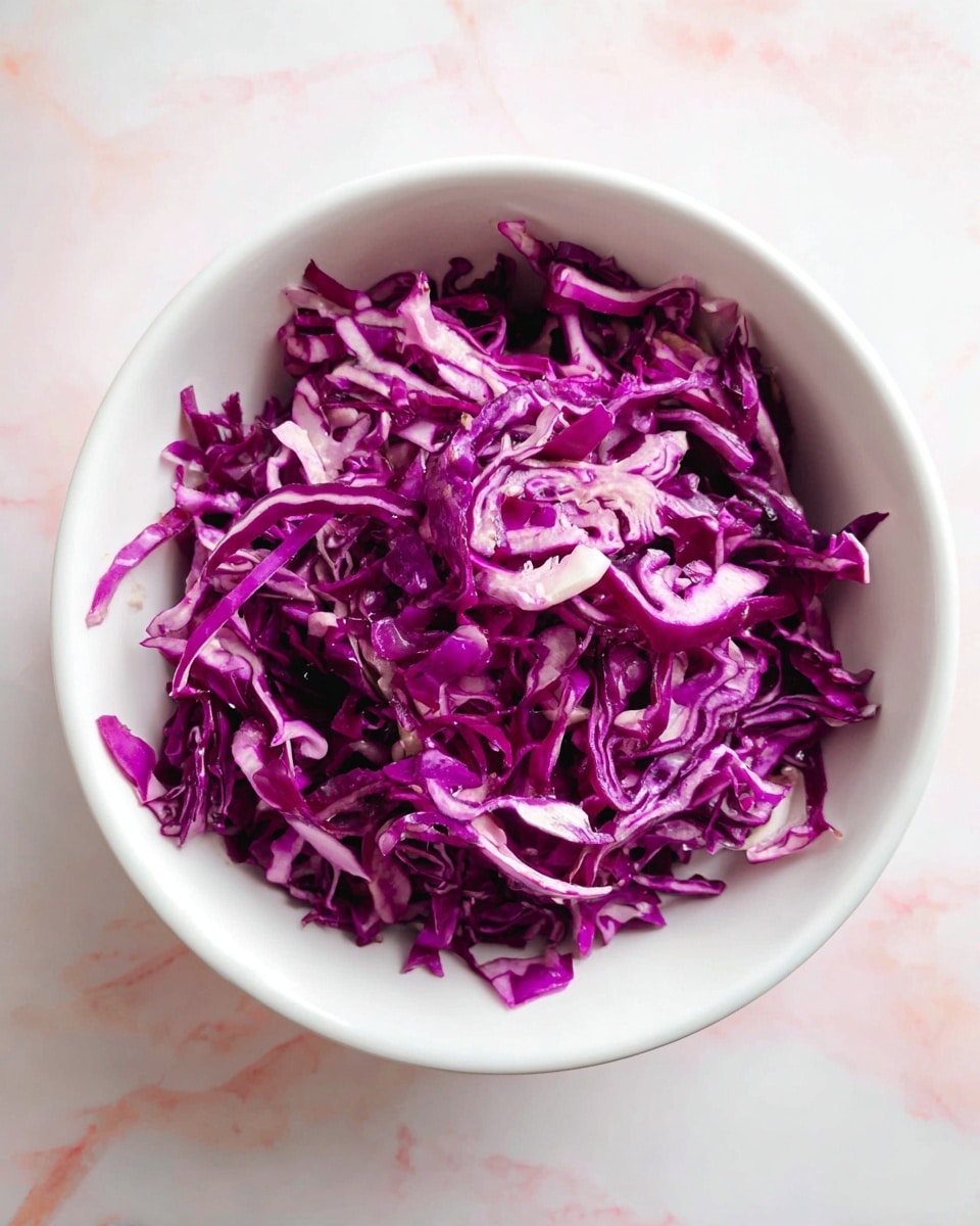 The image shows a white bowl filled with thin, shredded purple cabbage. The cabbage is bright purple with some white parts, creating a mix of wavy, curly textures throughout. The bowl sits on a surface with a white marbled texture. There is no other food or decoration visible around the bowl. photo taken with an iphone --ar 4:5 --v 7