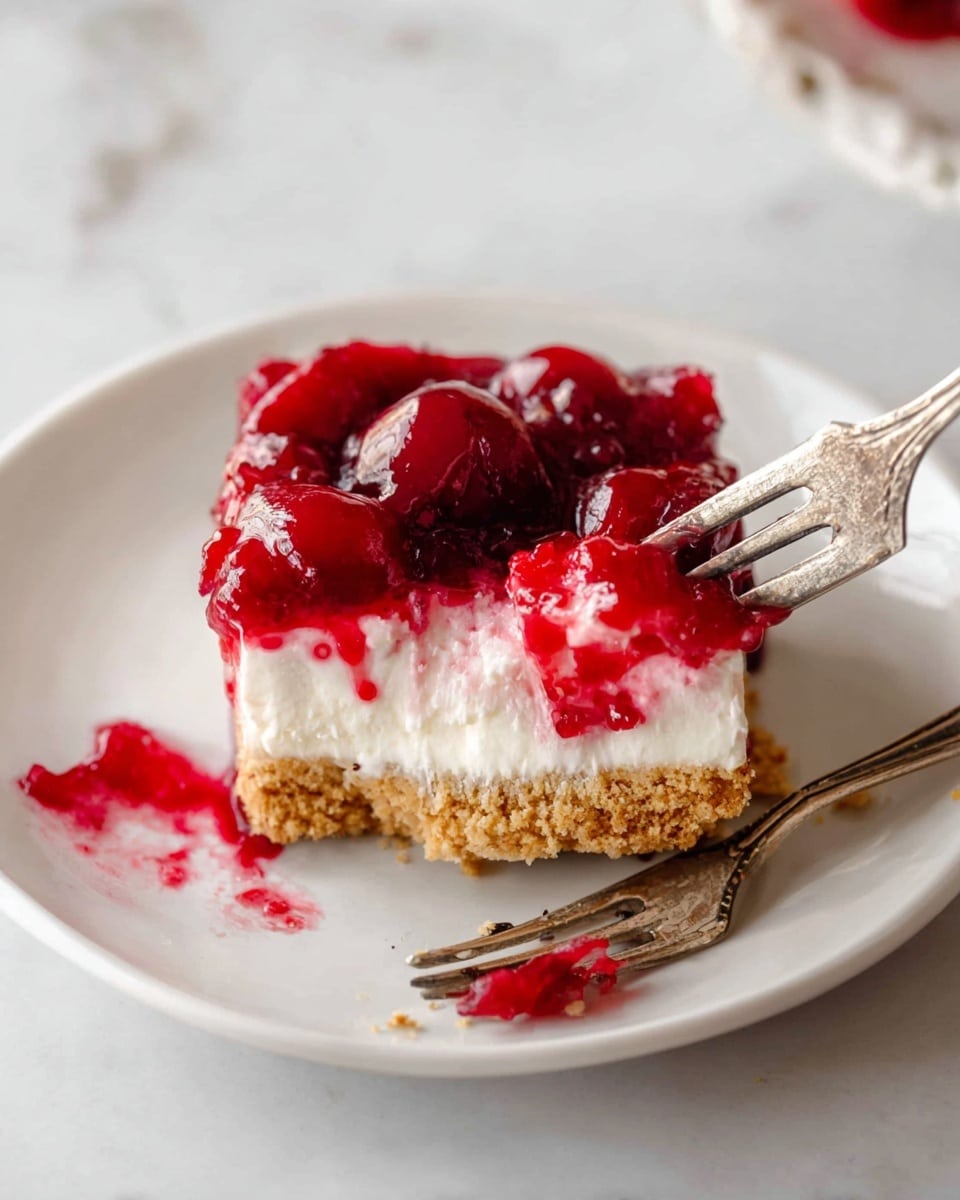 A slice of dessert on a white plate with three clear layers: the bottom layer is a light brown crumbly crust, the middle layer is thick and white creamy filling, and the top layer is a shiny, bright red cherry topping with whole cherries visible inside. A vintage silver fork holds a square piece of the dessert showing all three layers, with some red cherry topping spread on the plate. The background is a white marbled surface. Photo taken with an iphone --ar 4:5 --v 7
