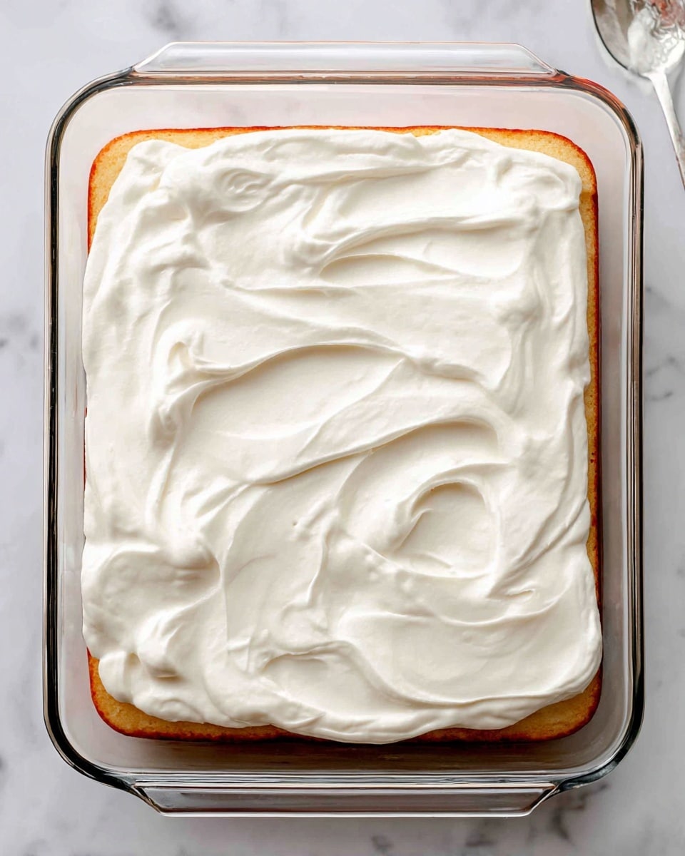 A single piece of light-colored sponge cake sits on a white plate with an ornate edge. The cake has one layer with a thick layer of white whipped cream on top. Fresh strawberry slices and whole blueberries are placed evenly on the cream, adding bright red and deep blue colors. A few berries also rest on the plate beside the cake. The plate is on a white marbled surface, and to the side of the plate is an old-fashioned silver fork. In the background, slightly out of focus, there is a dish with more strawberries and cream. photo taken with an iphone --ar 4:5 --v 7
