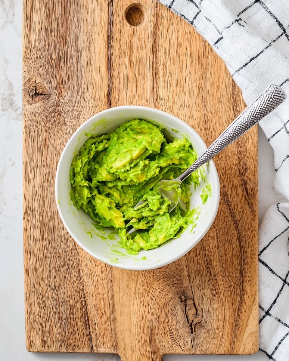 A white bowl holds a layer of dark purple tortilla chips arranged in a circle standing upright, creating a textured, spiky border. On top in the center is a thick scoop of chunky green guacamole mixed with small pieces of red tomato and flecks of green herbs. One yellow tortilla chip is dipped into the guacamole, sticking out from the center. The bowl is set on a white marbled surface with a blurred background of lime wedges. Photo taken with an iphone --ar 4:5 --v 7